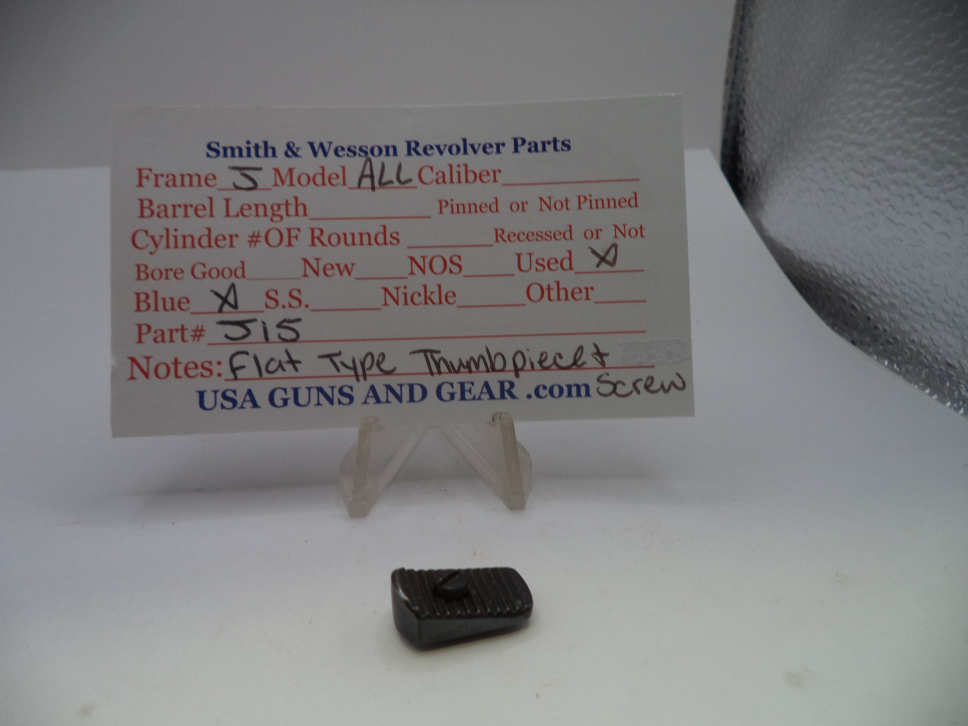 A small black metal screw part displayed below a printed parts information card for a Smith & Wesson revolver, on a white surface with a gray textured background.