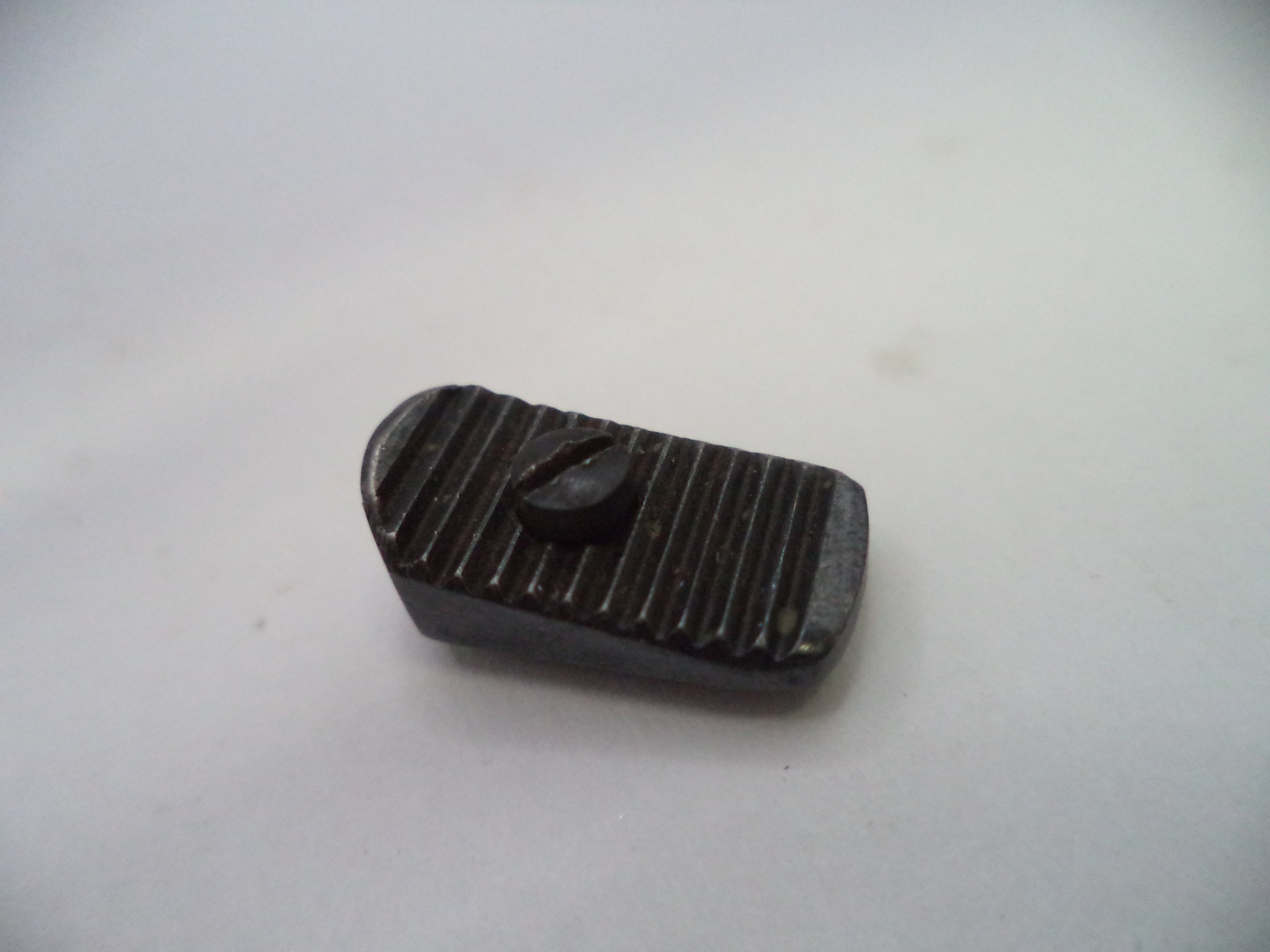 A small dark metal button with a ribbed rectangular face and a central oval depression, shown on a plain light background.
