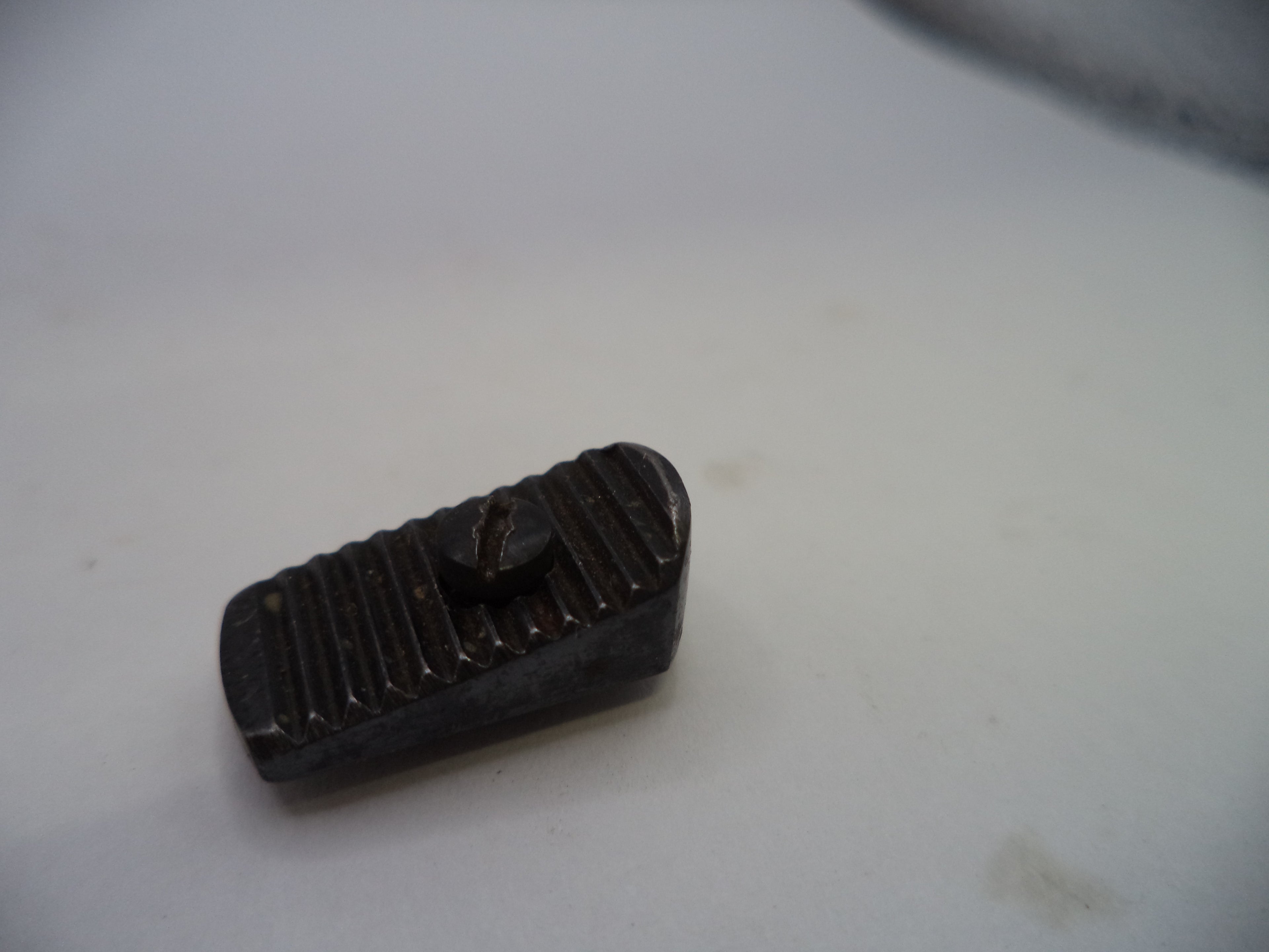 A small dark metal or plastic rectangular component with a ribbed top surface and a small protruding tab, photographed on a plain light background.