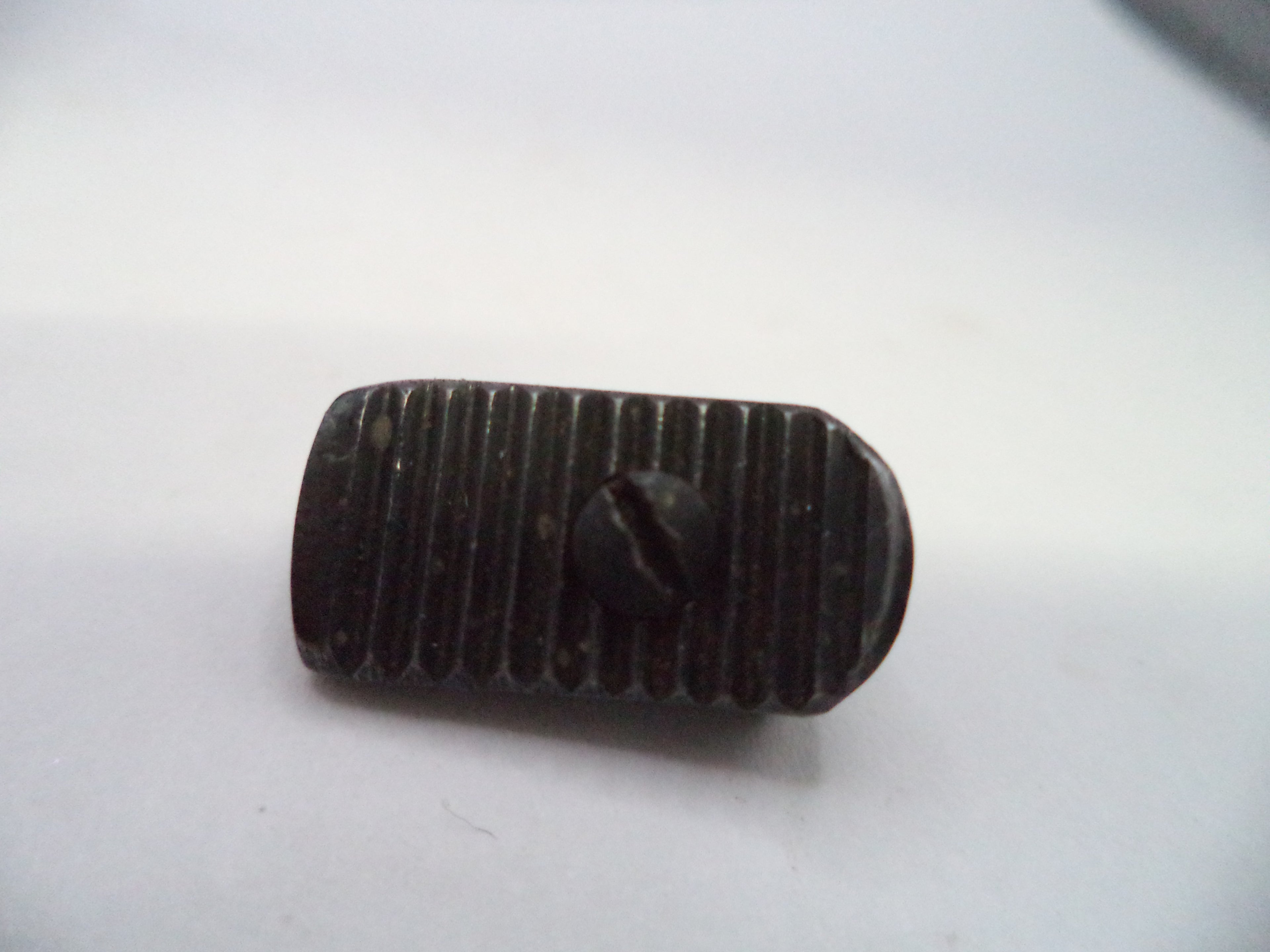 A small dark metal button with a ribbed texture and a central screw head, shown on a plain light background.