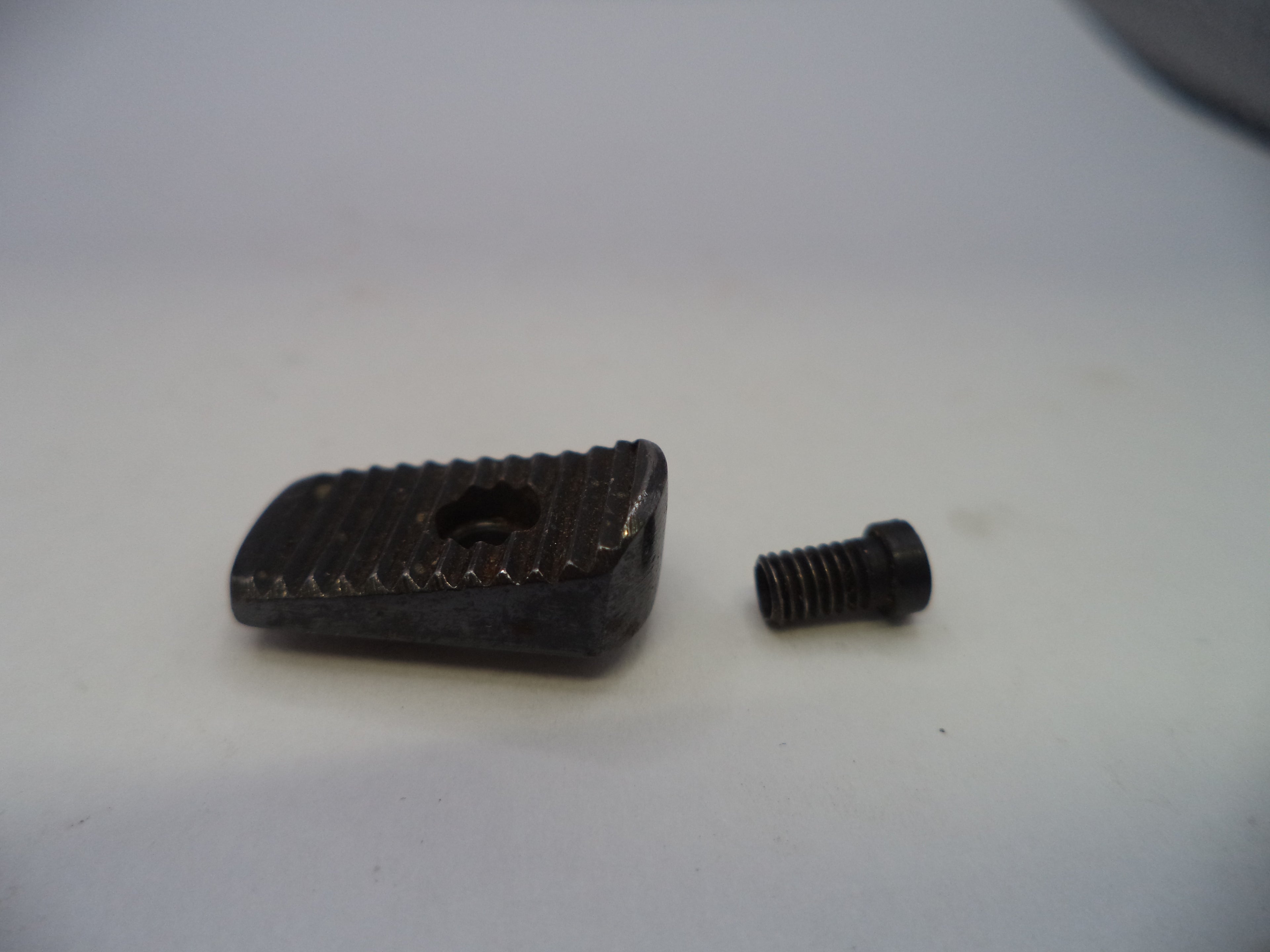 A small black metal adjustment block with a textured surface and a central hole, shown next to a matching black threaded screw on a plain light background.