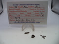 Smith & Wesson revolver lock parts displayed on a white surface with a handwritten parts card. The set includes a small metal screw, a dark metal lock component, and a small metal key, shown on clear plastic stands.