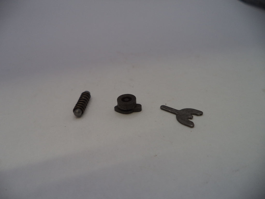 Three small mechanical parts, including a coil spring, a small black plastic or rubber piece, and a small metal clip, arranged on a plain light gray surface.