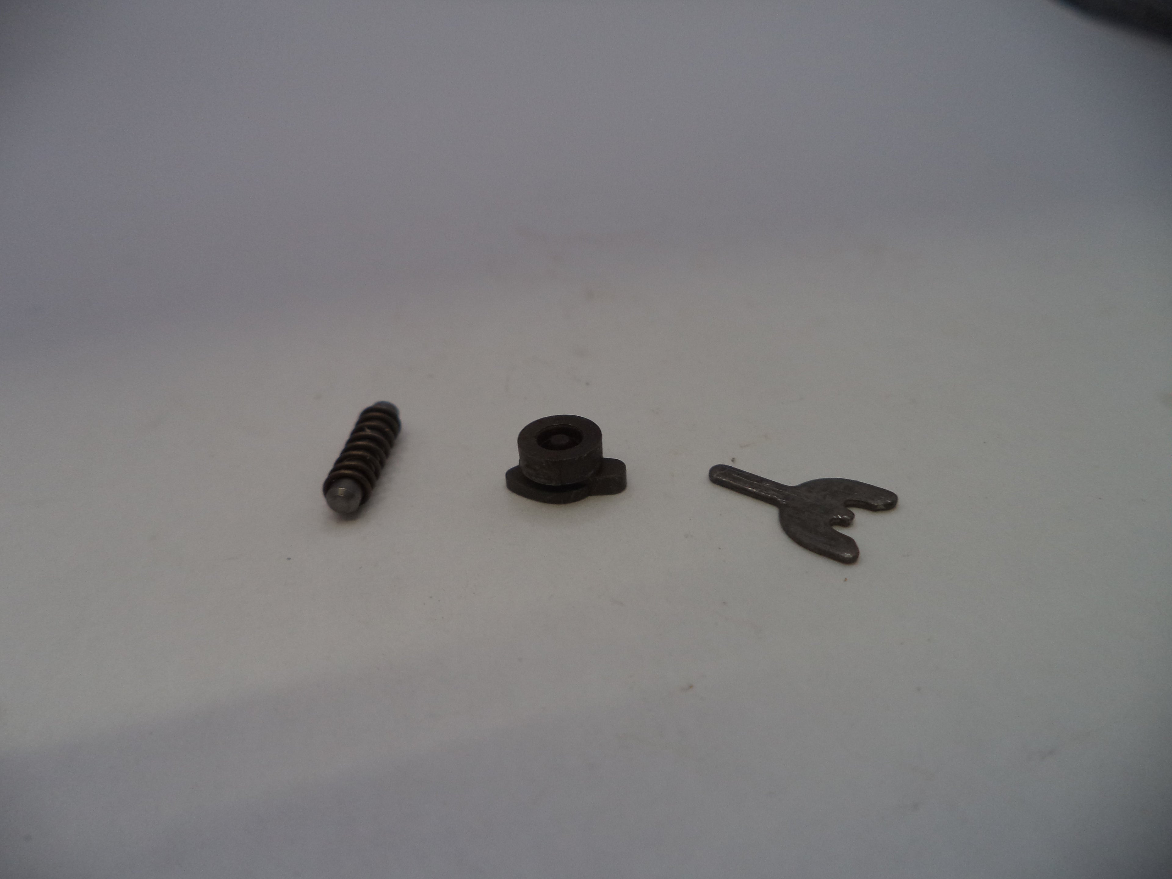 Three small mechanical parts, including a coil spring, a small black plastic or rubber piece, and a small metal clip, arranged on a plain light gray surface.