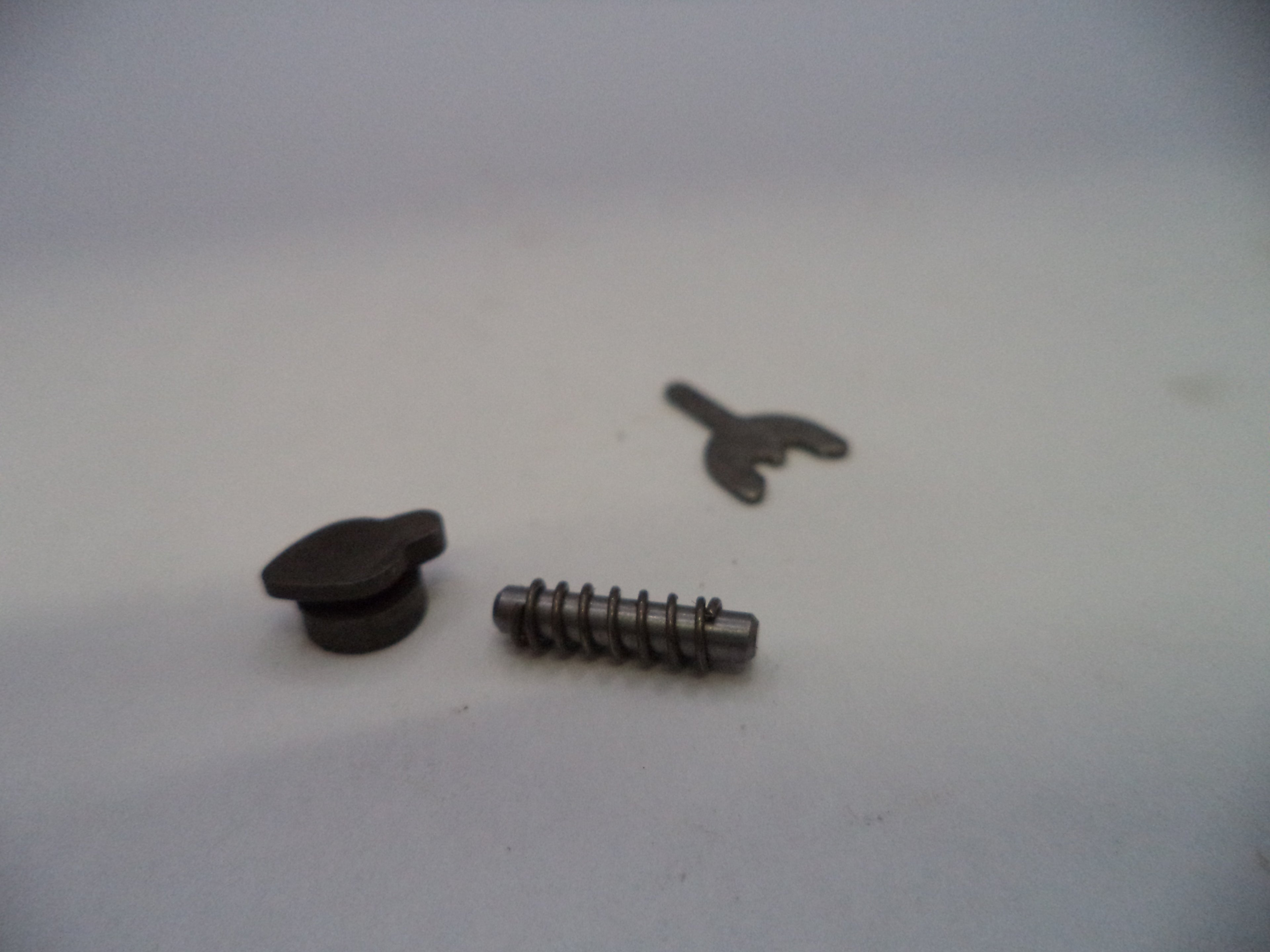 A small metal hardware set consisting of a dark metal snap button, a silver metal screw pin, and a small metal clip, displayed on a plain light gray surface.