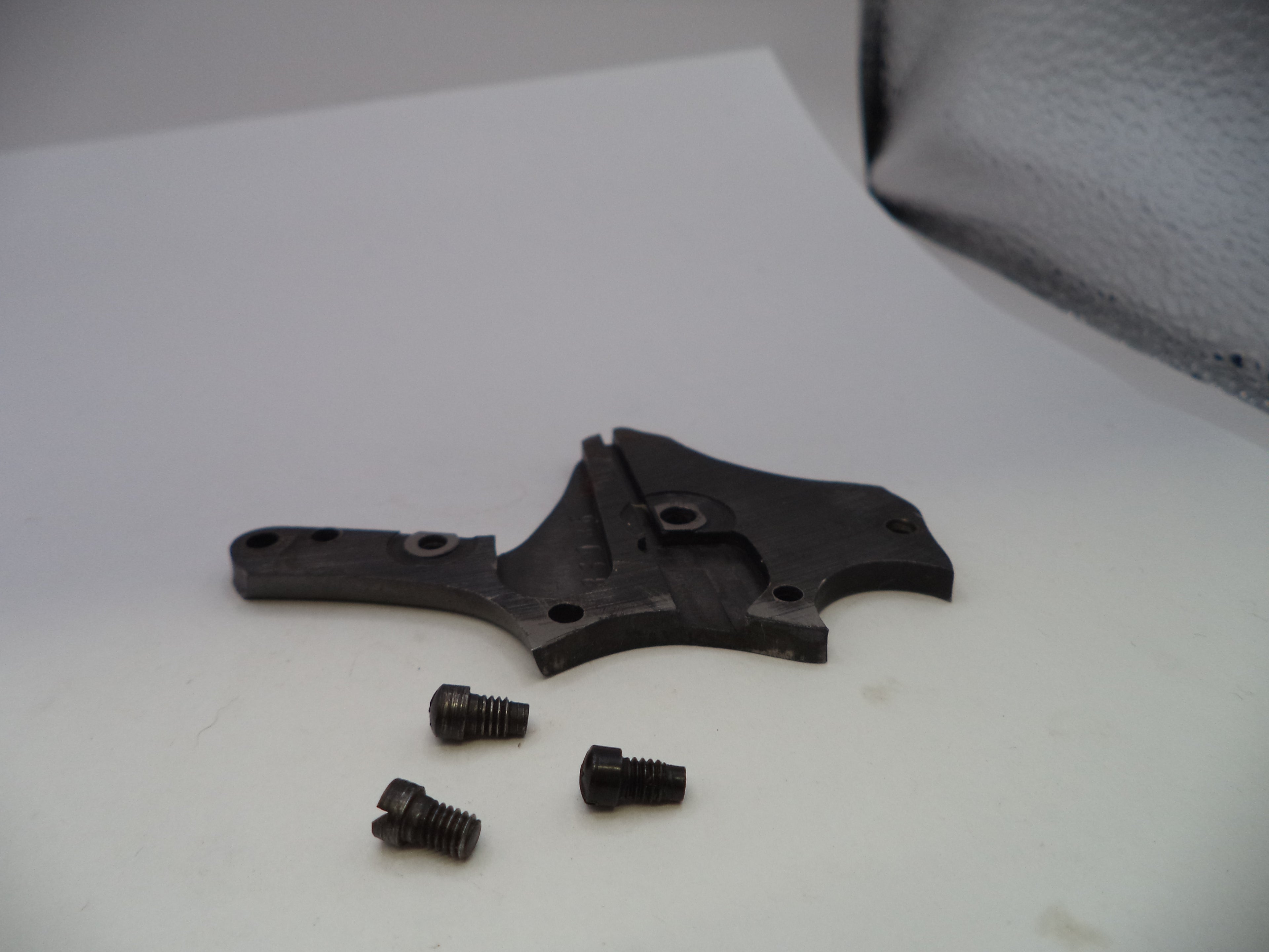A dark metal mechanical component with three small matching screws, displayed on a white surface.