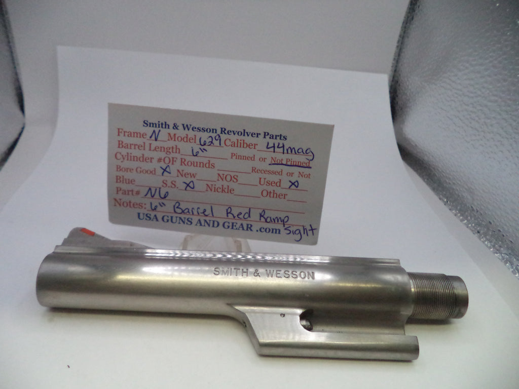 A Smith & Wesson revolver cylinder block part made of stainless steel, displayed on a white surface with a handwritten parts identification card behind it.