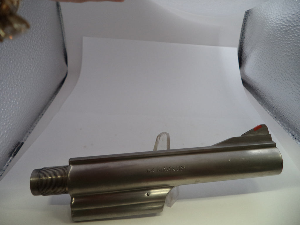 A metallic cylindrical gun stock or receiver component with a threaded end and a small red accent on the rear, photographed on a white studio sweep with textured light boxes visible at the sides.