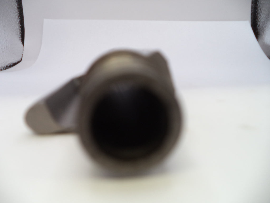A close-up, heavily blurred shot of a dark metallic cylindrical object, possibly a mechanical part or tool, resting on a white surface.