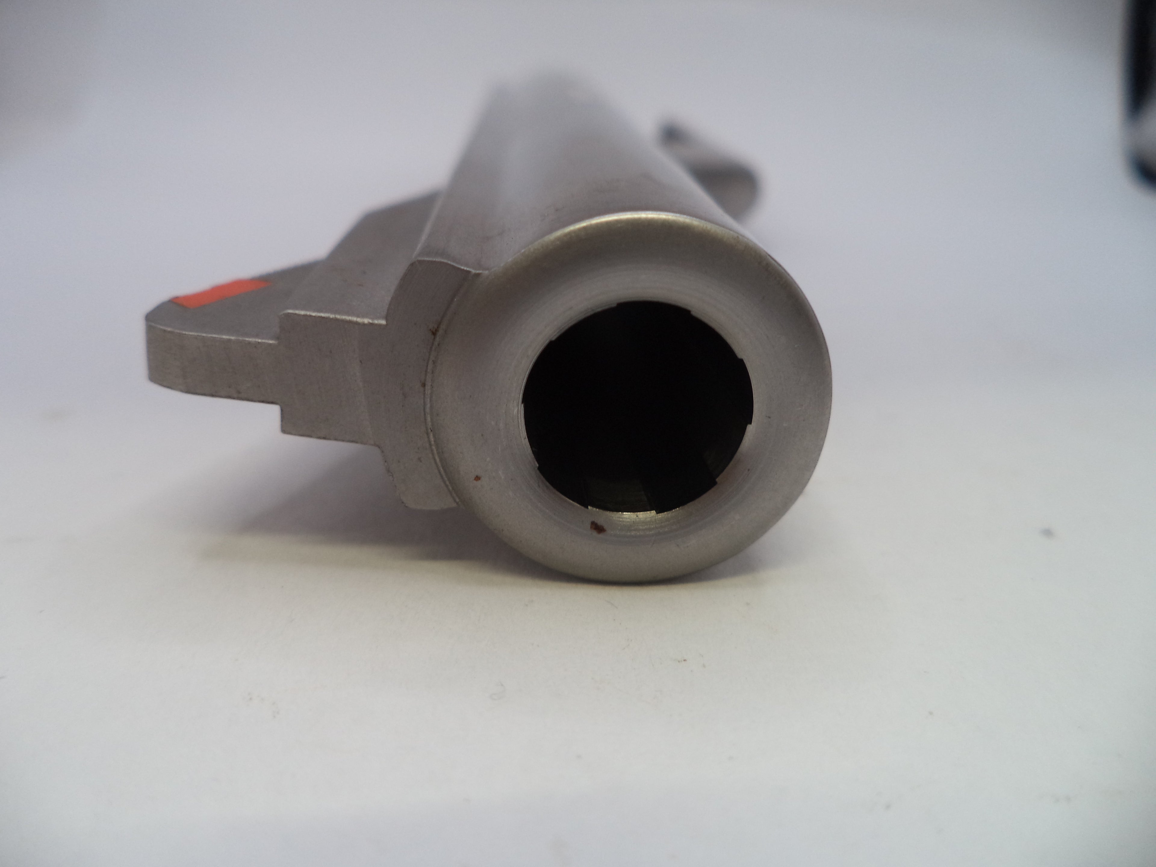 A close-up shot of a metallic gray cylindrical component, showing a circular opening and a small red marking on the side, set against a plain white background.