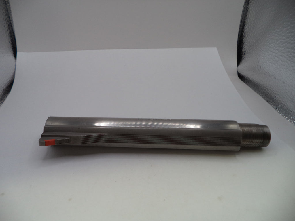 A cylindrical metal cutting tool or drill bit with a fluted shank and a small orange accent near the cutting edge, photographed on a white surface with a reflective silver backdrop.