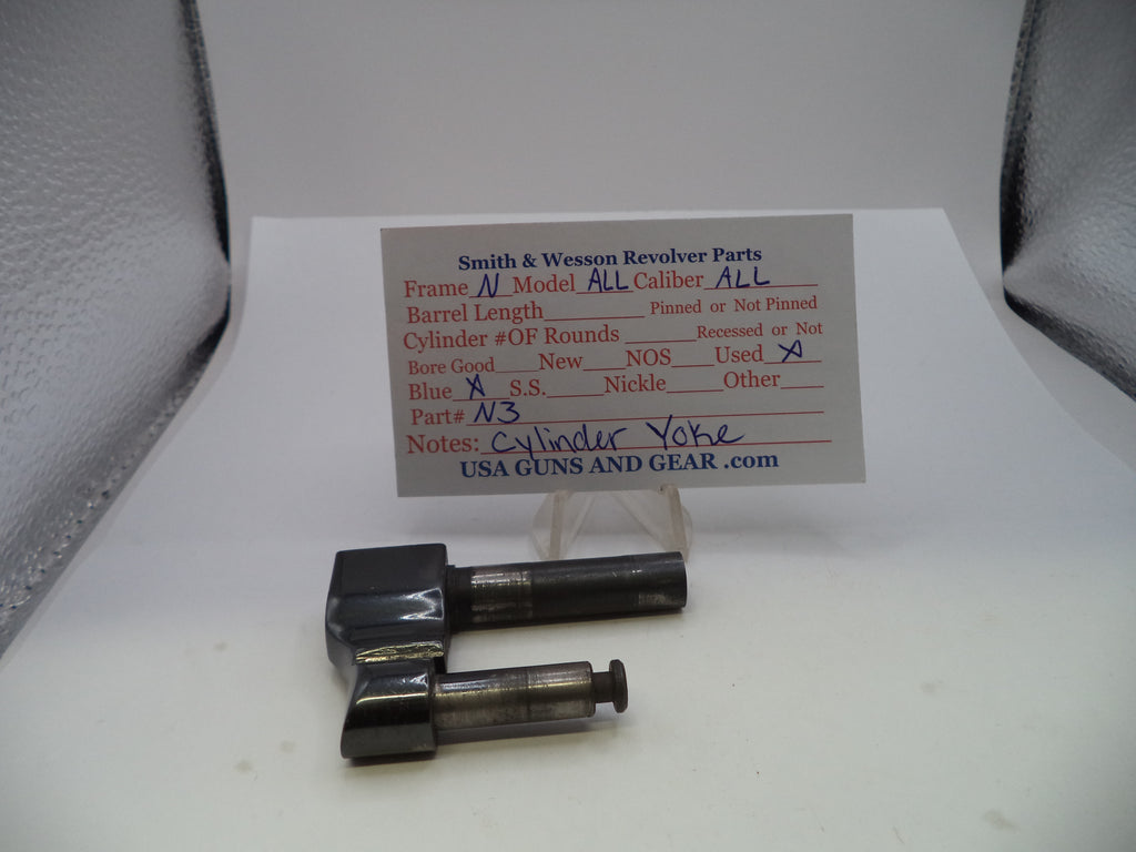 Two metal revolver cylinder blocks with blackened finishes displayed on a white surface in front of a printed parts information card. The card reads Smith & Wesson Revolver Parts and includes fields for caliber, barrel length, and condition.