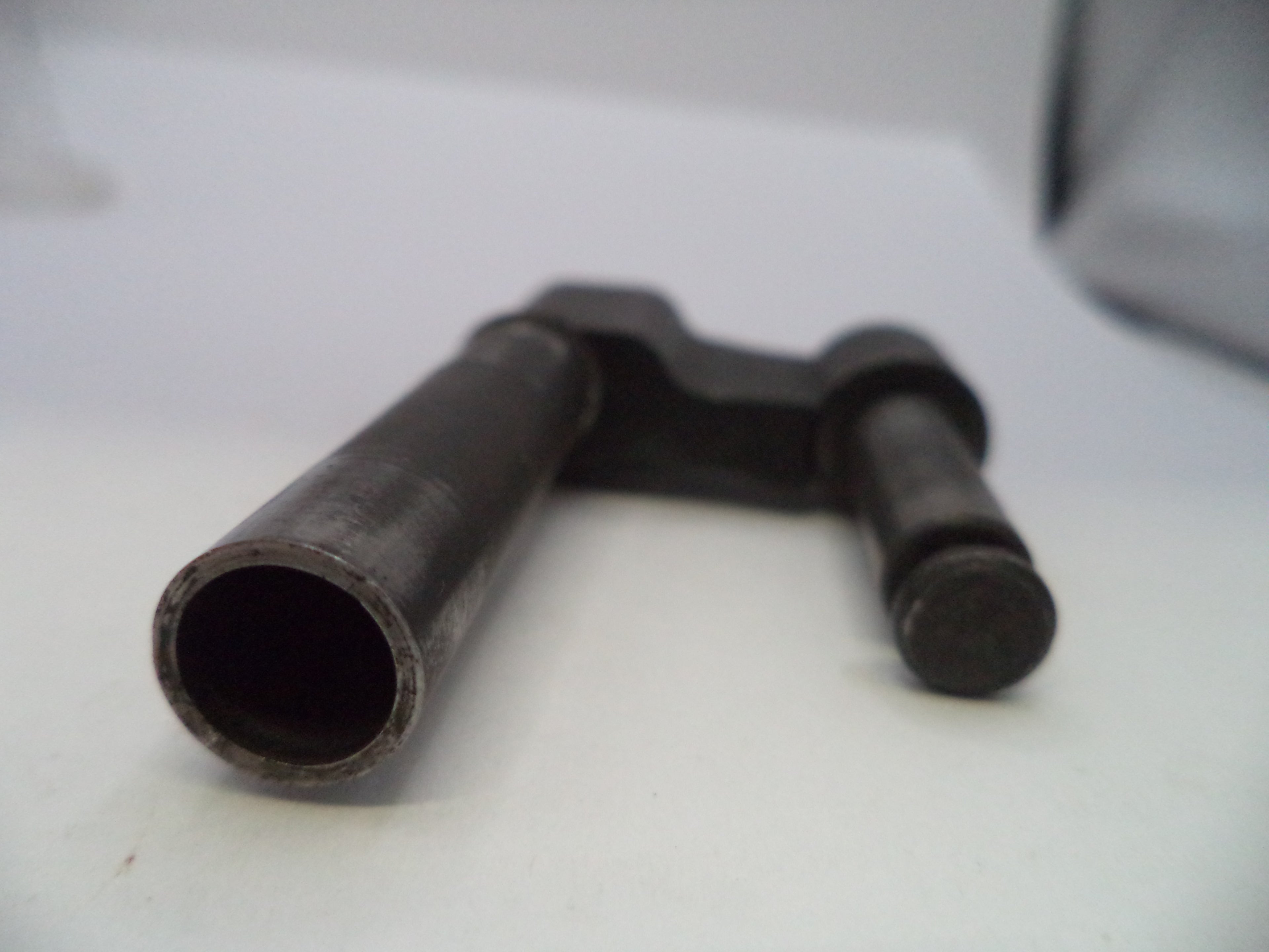 A dark metal mechanical part, possibly a valve stem or guide rod, resting on a white surface.