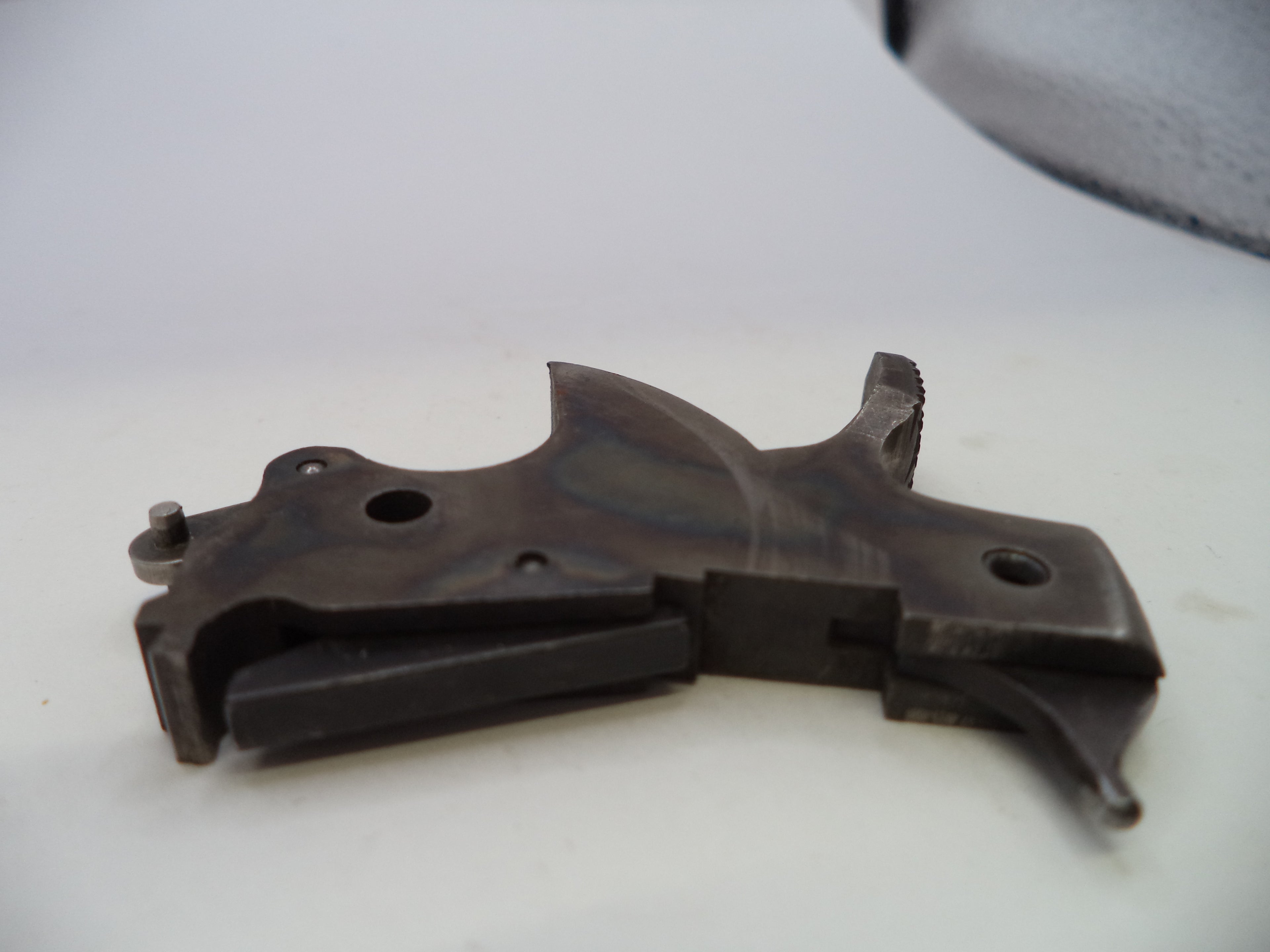 A dark metallic gun trigger assembly, likely made of steel or iron, photographed on a plain white surface.