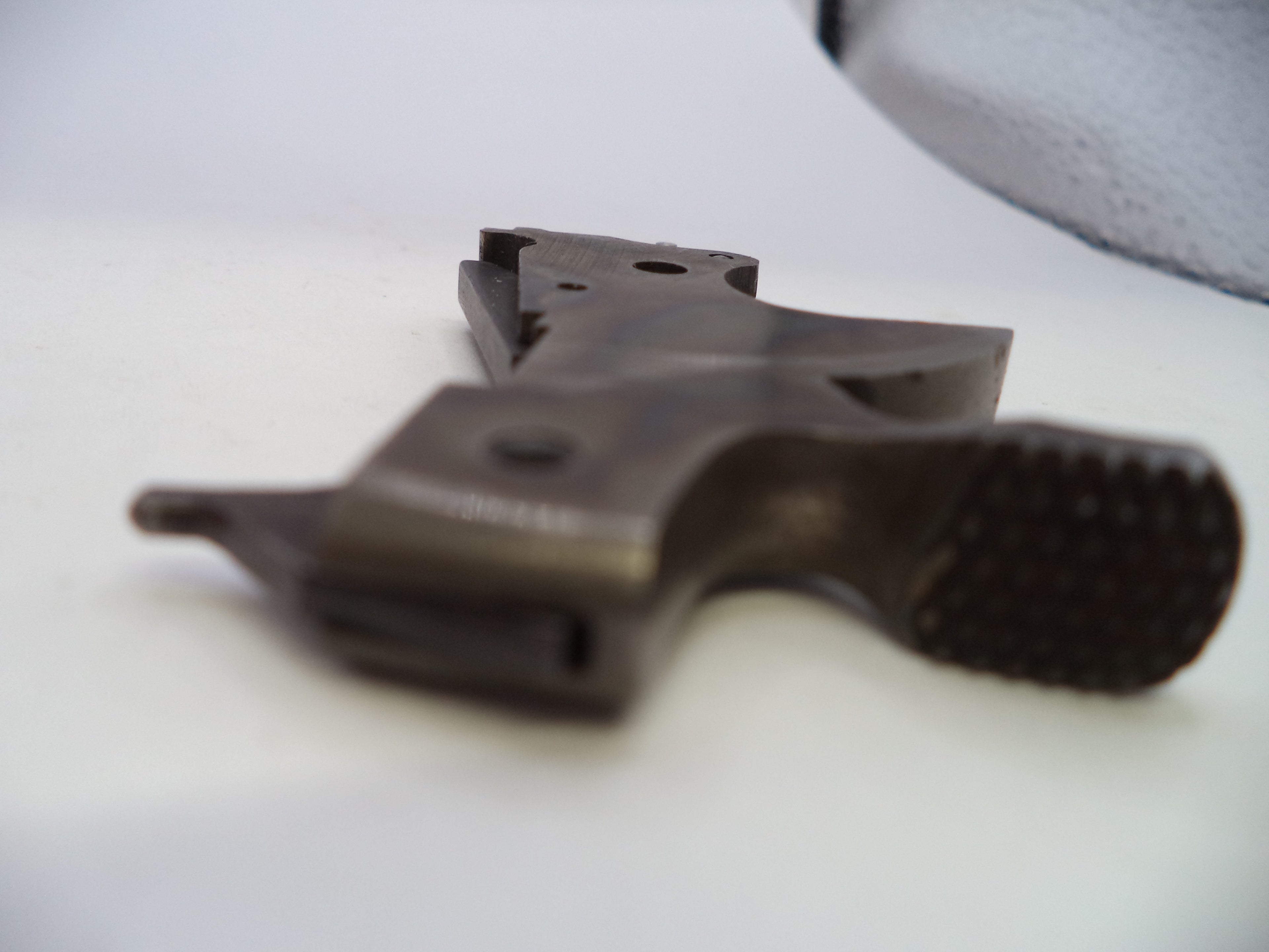 A close-up of a dark metallic gun grip component with a textured rubberized end, photographed on a white surface.