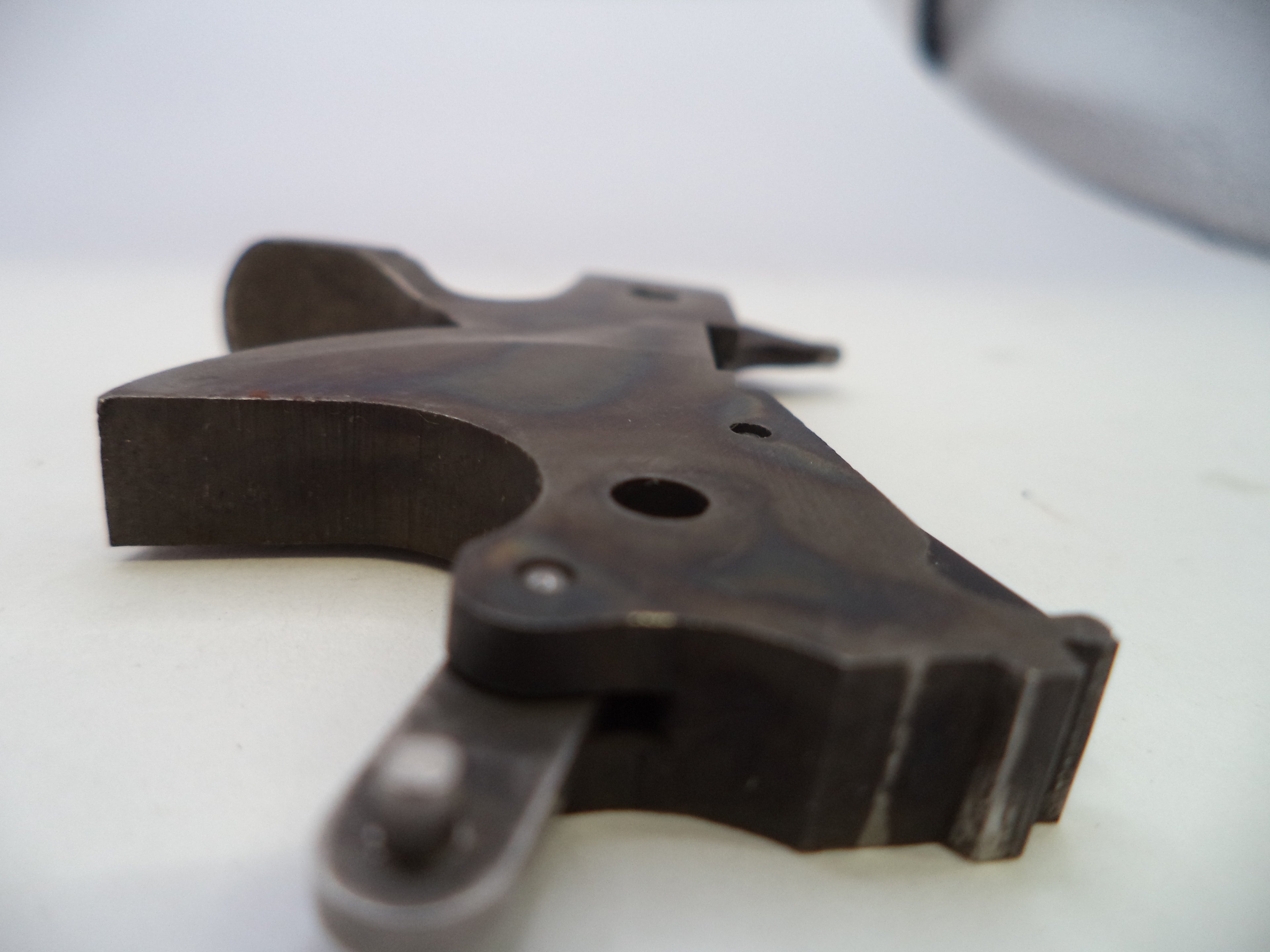 A close-up of a dark metal firearm accessory, likely a receiver or grip component, on a plain light background.