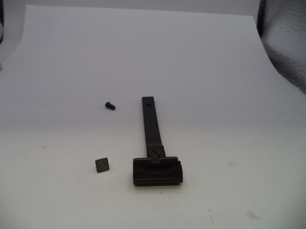 A black metal tool or hardware piece with a long handle and a textured head, shown on a white surface with two small detached parts nearby.