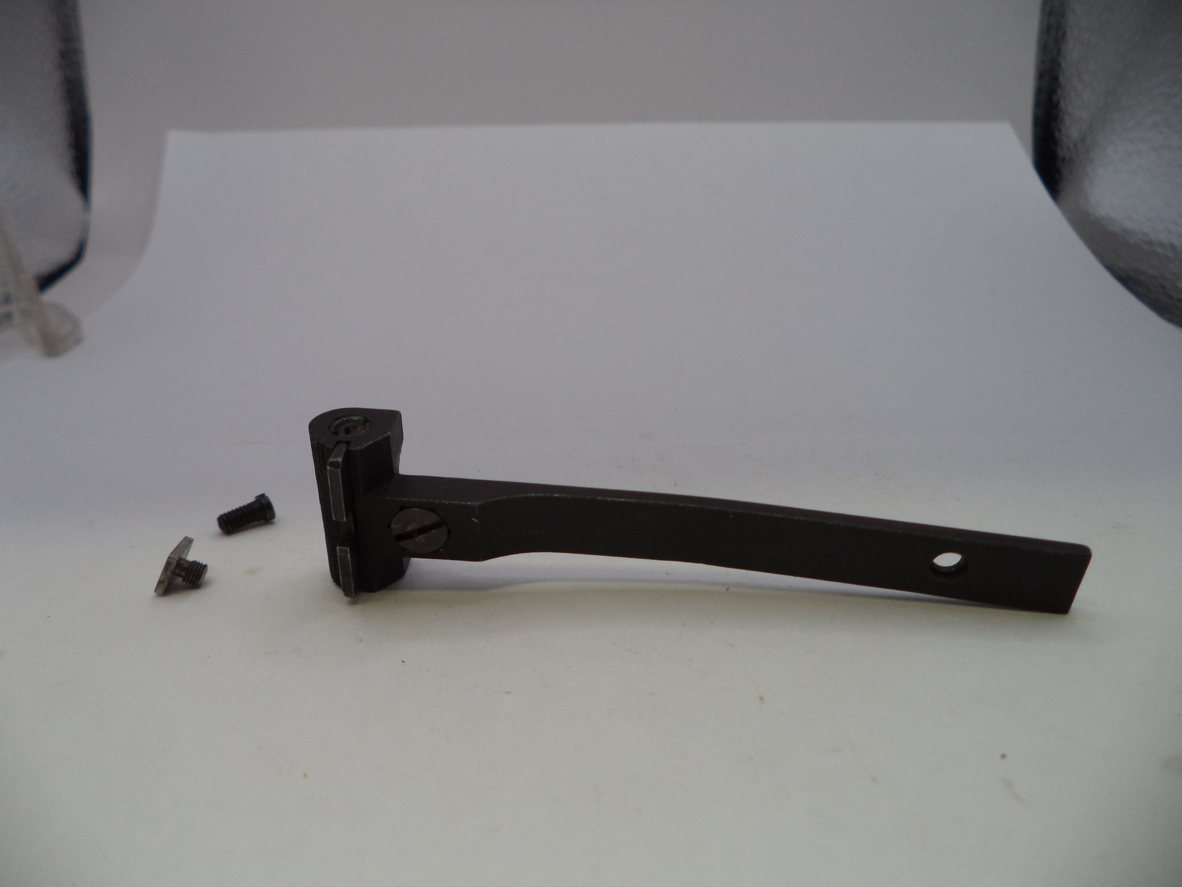 A black metal lever or handle with a small mounting hole on one end, shown on a white surface with two small metal screws beside it.