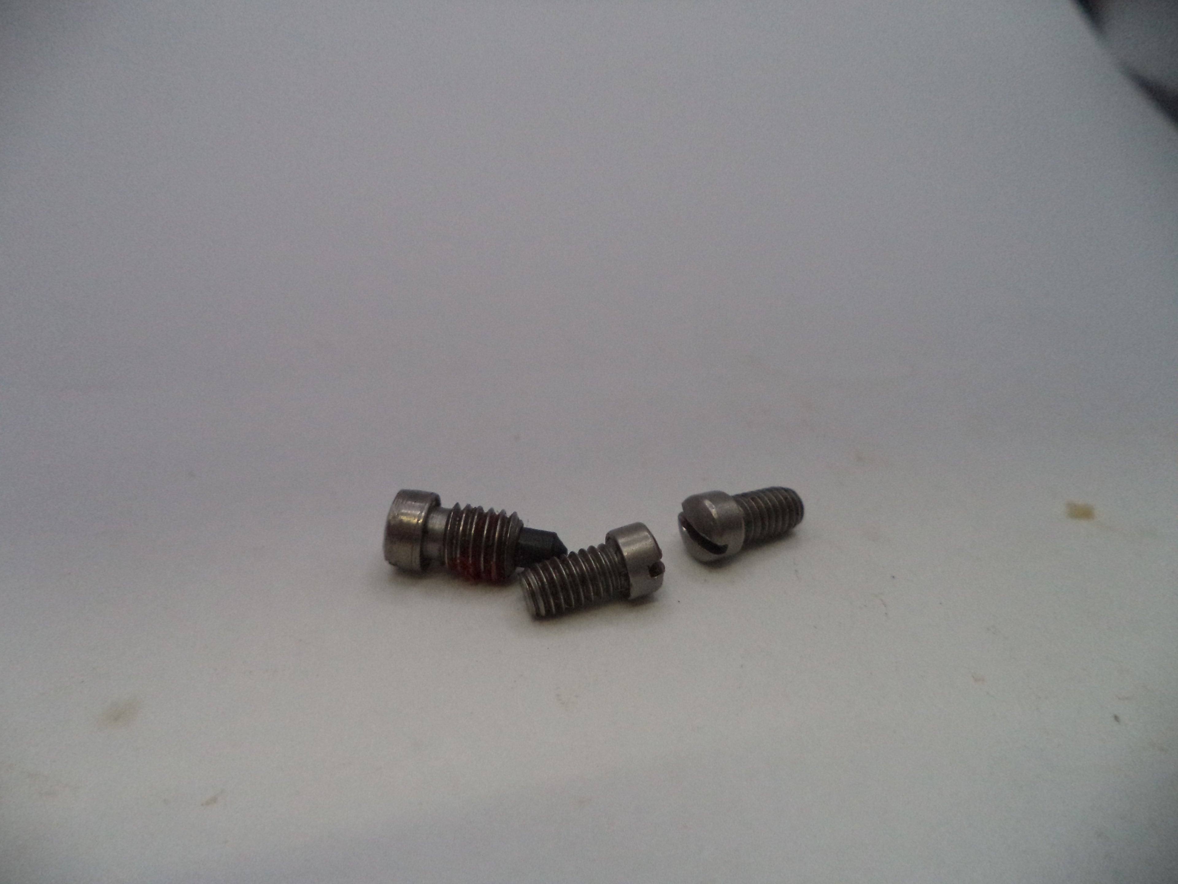 Three small metallic threaded screws or bolts with hex heads, displayed on a plain off-white surface.
