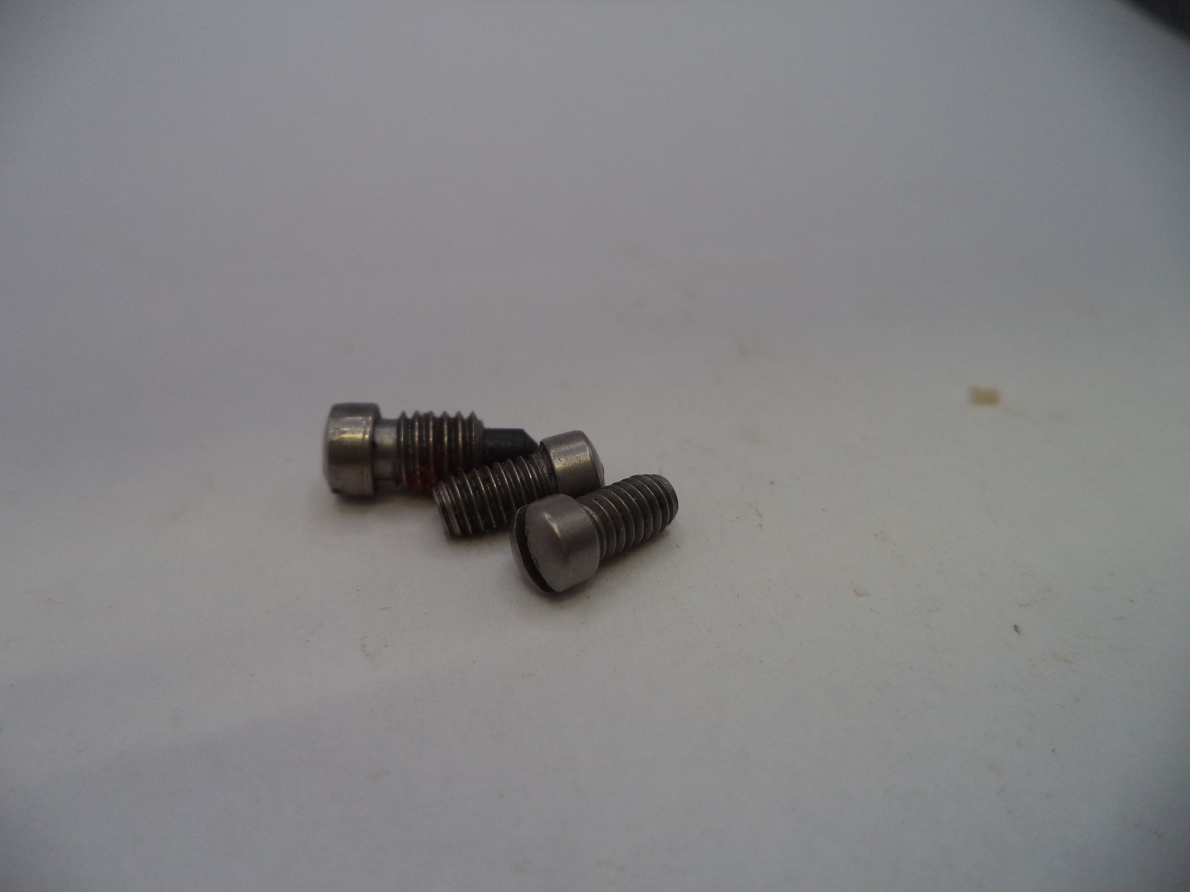 Three small metallic screws with hex heads and threaded shanks, photographed on a plain light background.