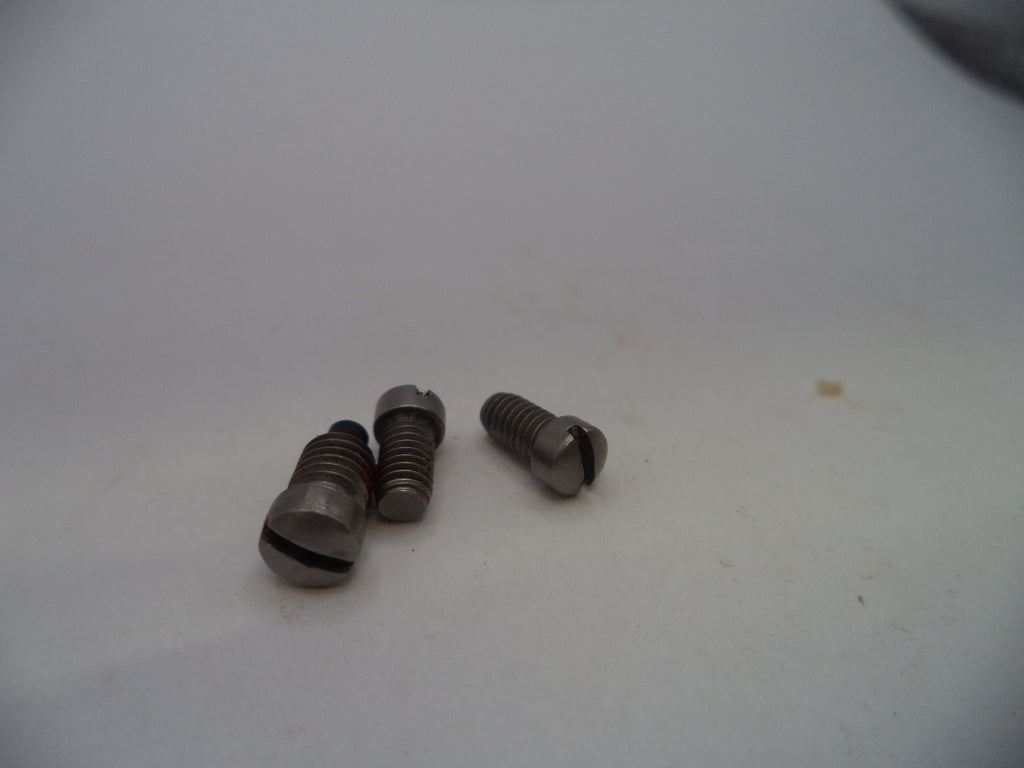 Three small metallic screws with slotted cross-drilled heads, showing a dark metallic gray finish, resting on a plain off-white surface.
