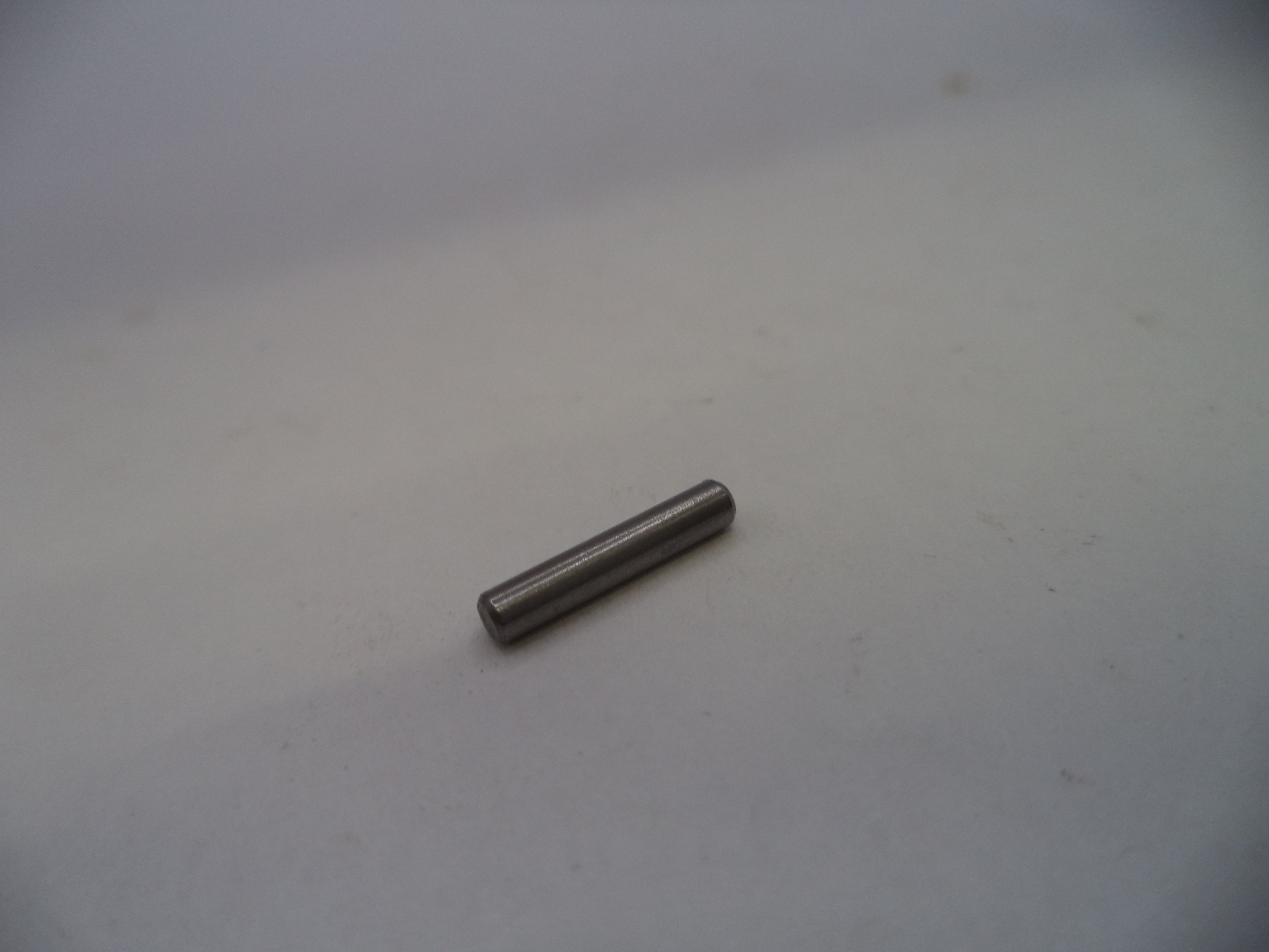 A small metallic cylindrical pin or rod lying on a plain light gray surface.