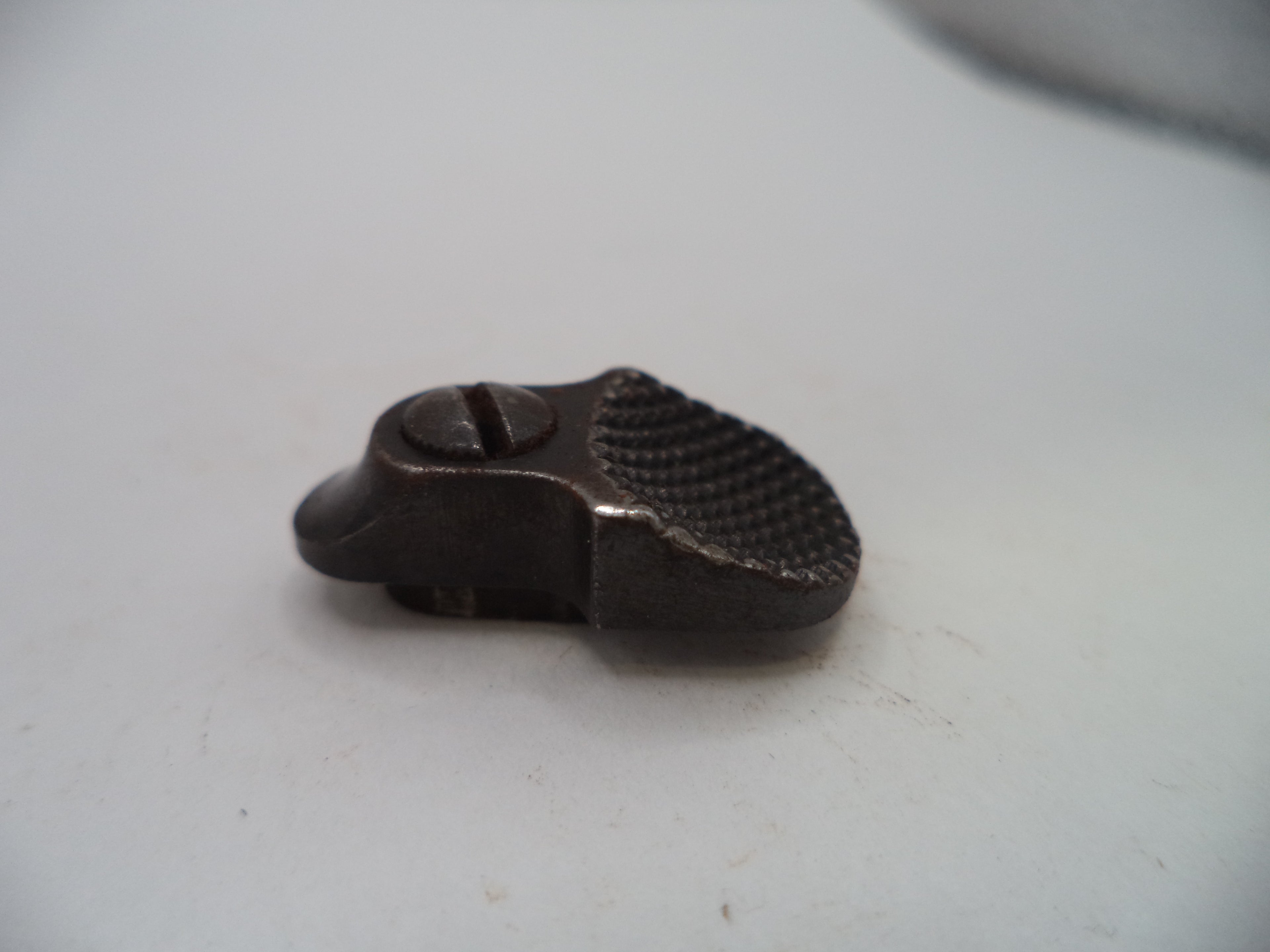 A small dark metal hardware piece with a textured grip and a slotted screw, photographed on a plain light background.