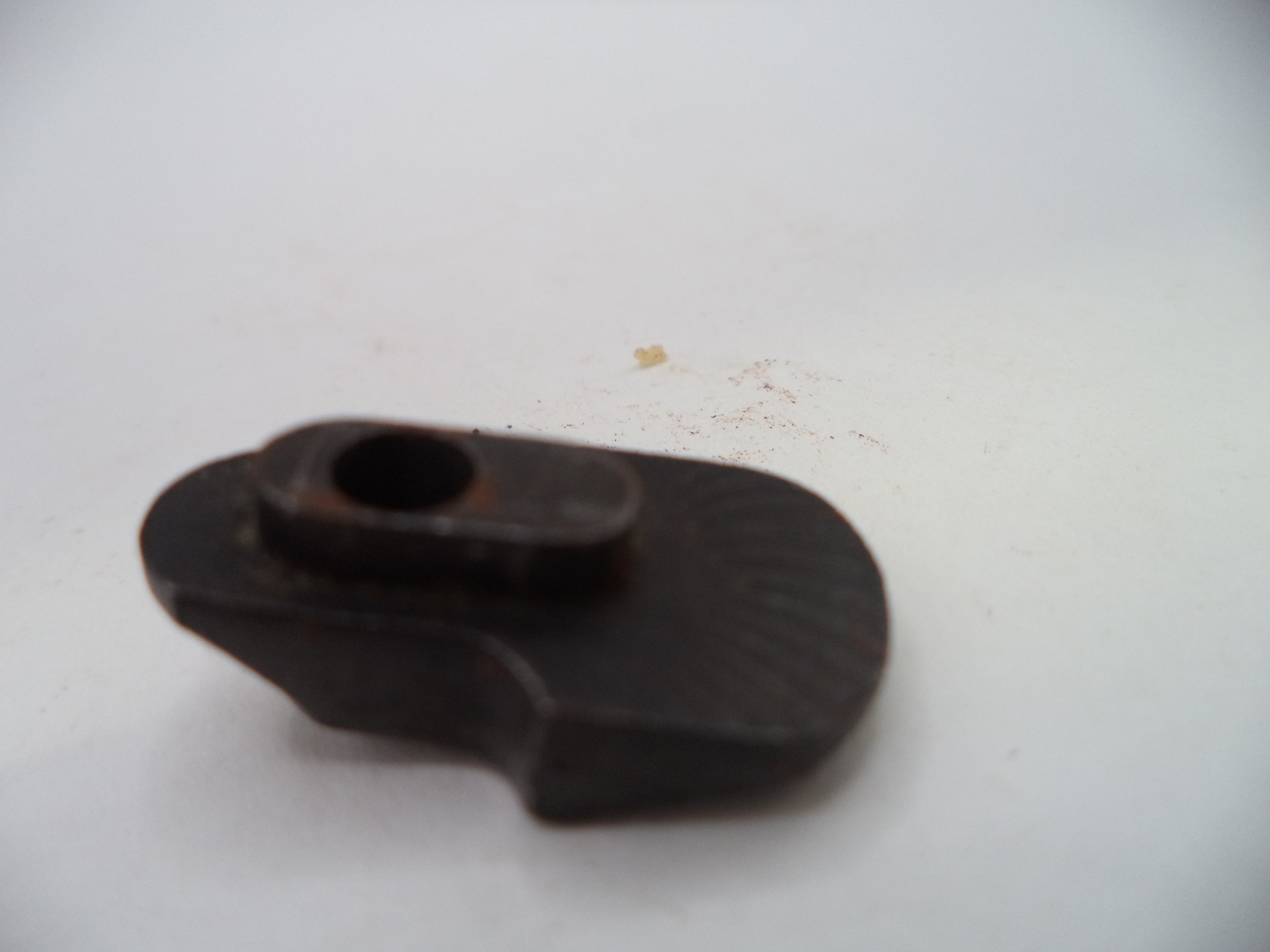 A small dark metal mechanical component with a circular hole, photographed on a plain off-white surface.