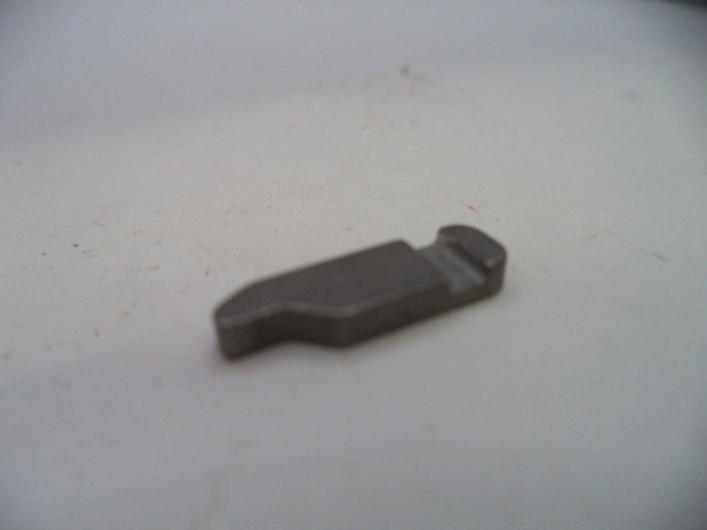 A small, dark gray metal replacement part, possibly a valve or clip, resting on a plain off-white surface.