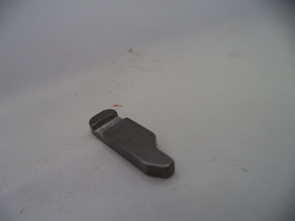 A small dark gray metal replacement part, possibly a clip or bracket, resting on a light gray surface.