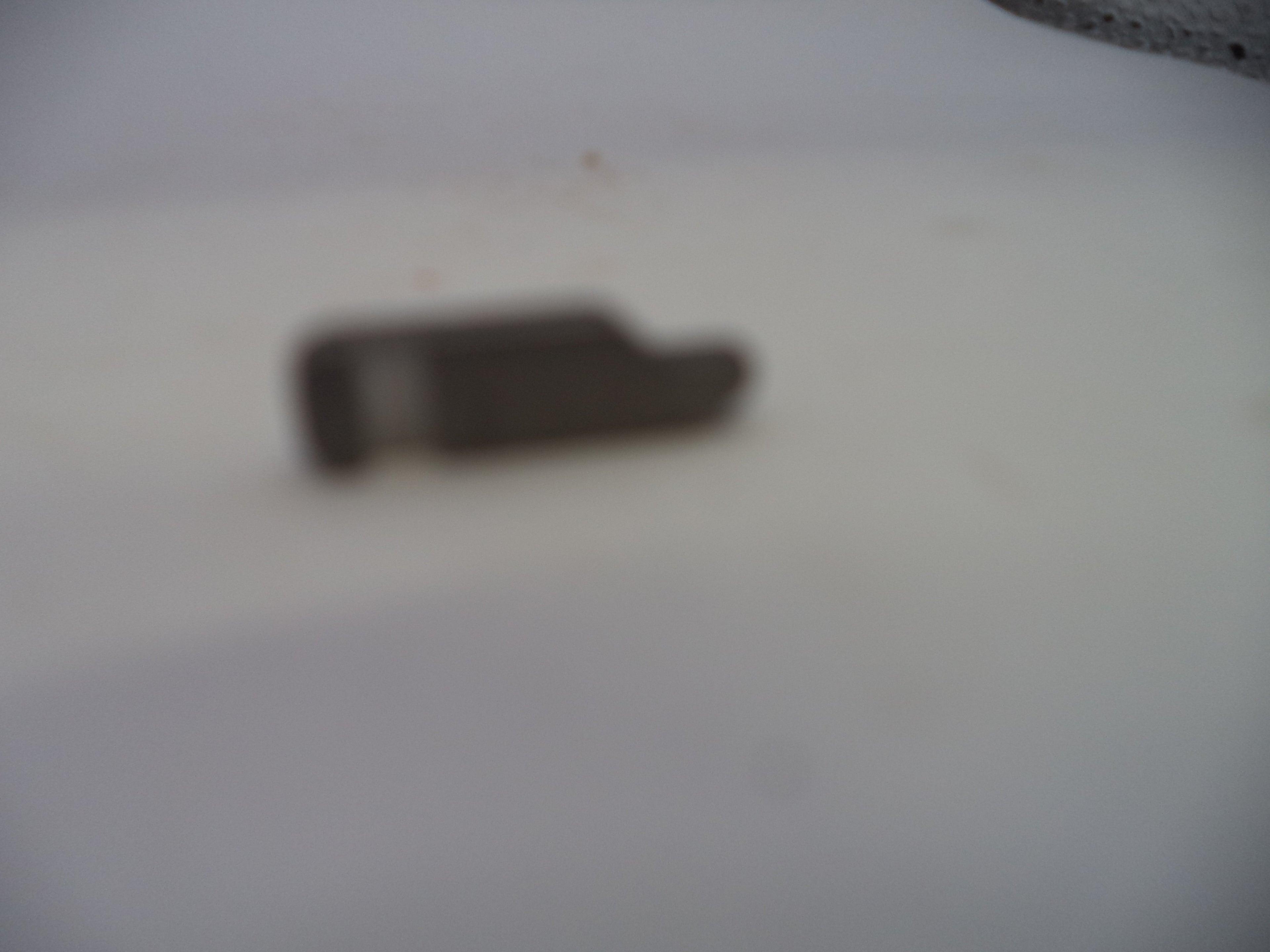 A small, blurry dark gray metal component resting on a plain white surface.