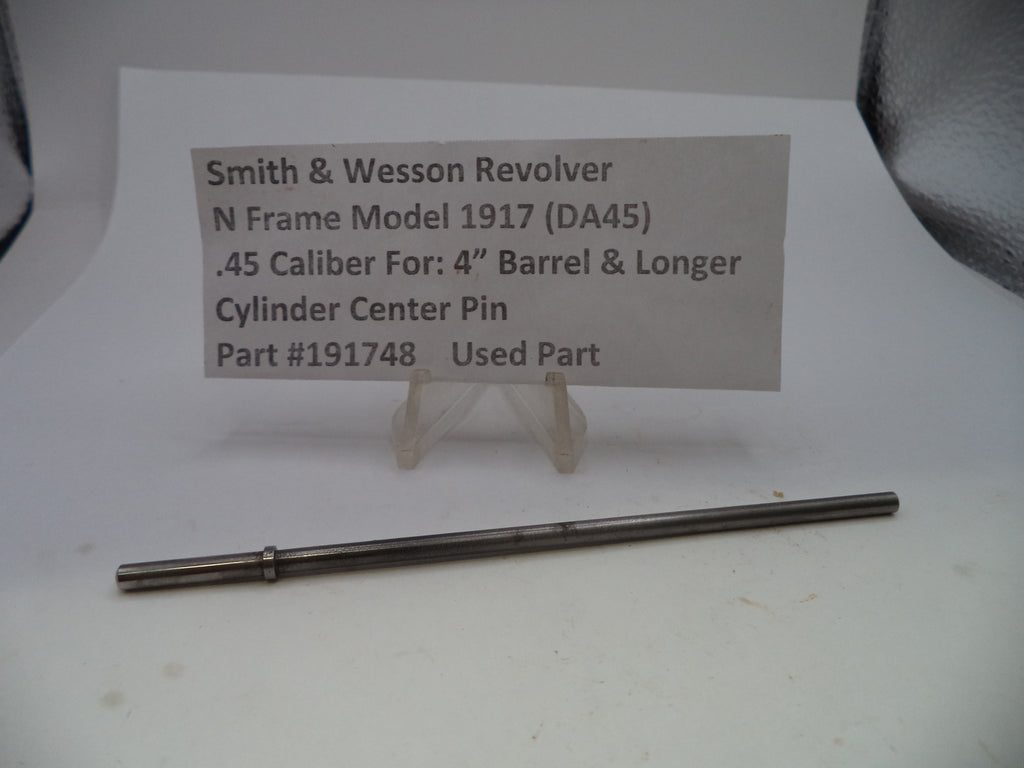 A used metal cylinder center pin for a Smith & Wesson revolver, displayed on a white surface below a paper label card with part details.