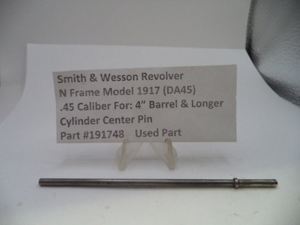 A used metal cylinder center pin for a Smith & Wesson revolver, displayed on a white surface below a paper label card with part details.