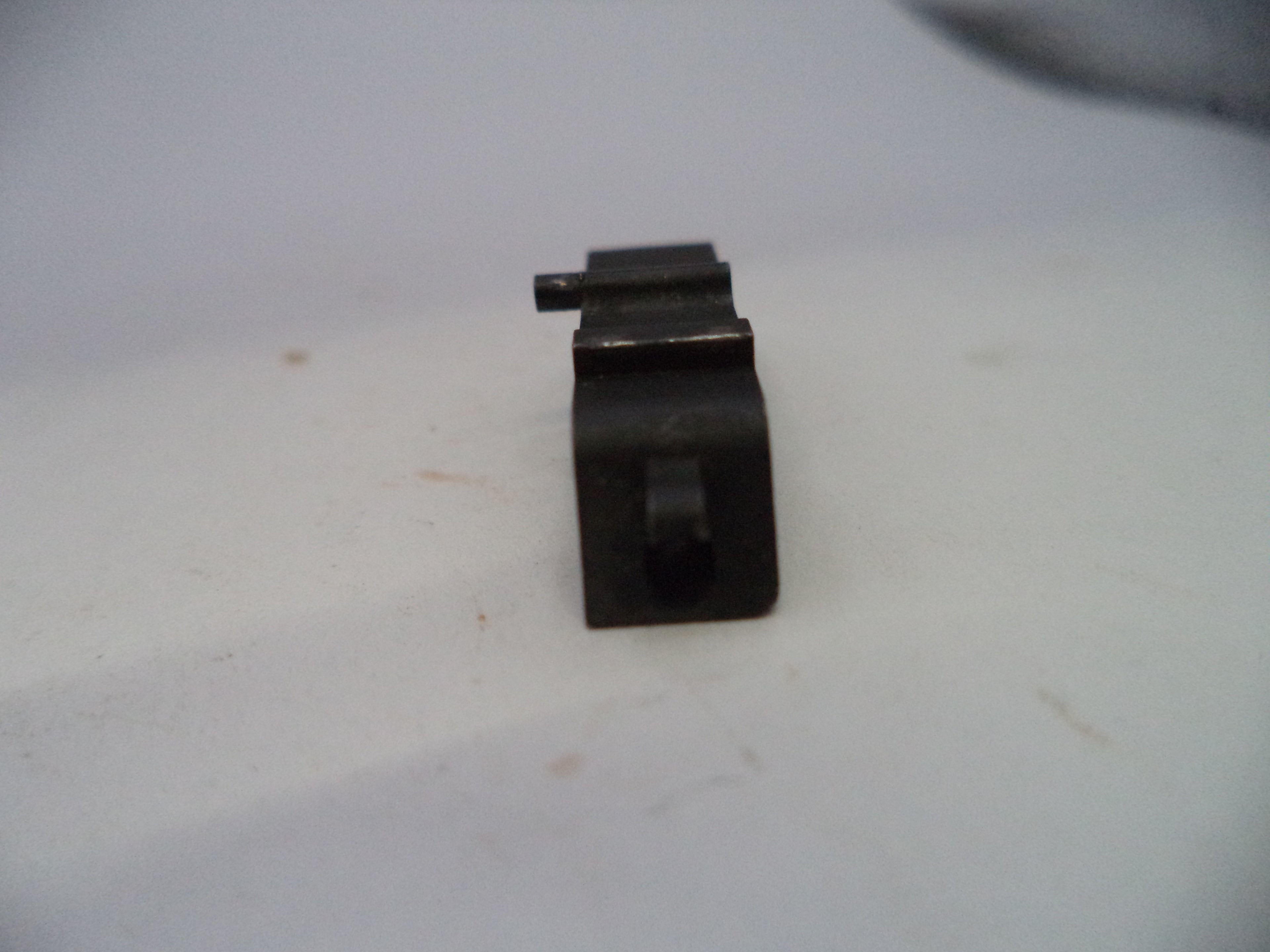 A small black metal hardware component, possibly a bracket or mounting piece, shown on a plain off-white surface.