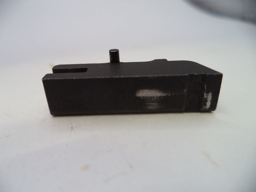 A black metal mechanical component, likely a receiver or magazine body, with a small protruding pin and a rectangular slot, shown on a light gray background.