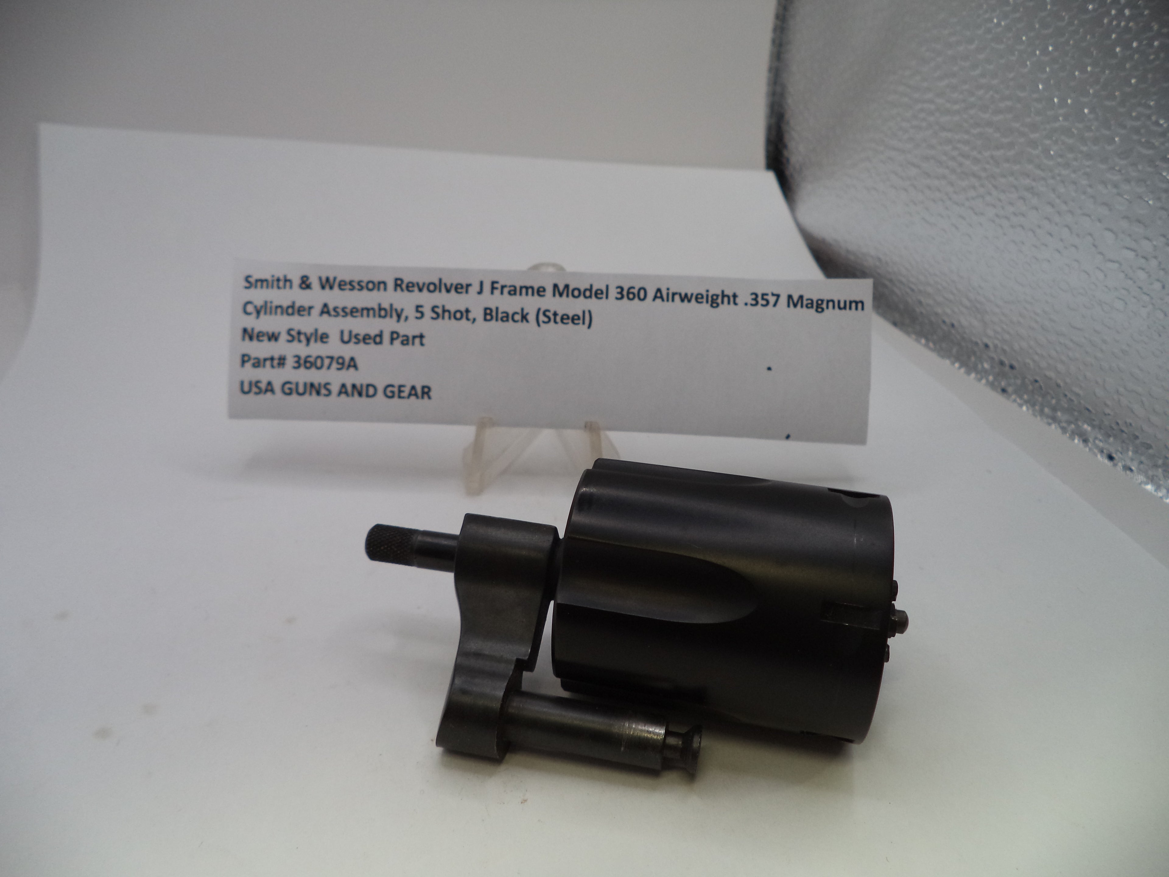 A black metal cylinder assembly part for a Smith & Wesson Revolver J Frame Model 360 airgun, displayed on a white surface with a product information card behind it.