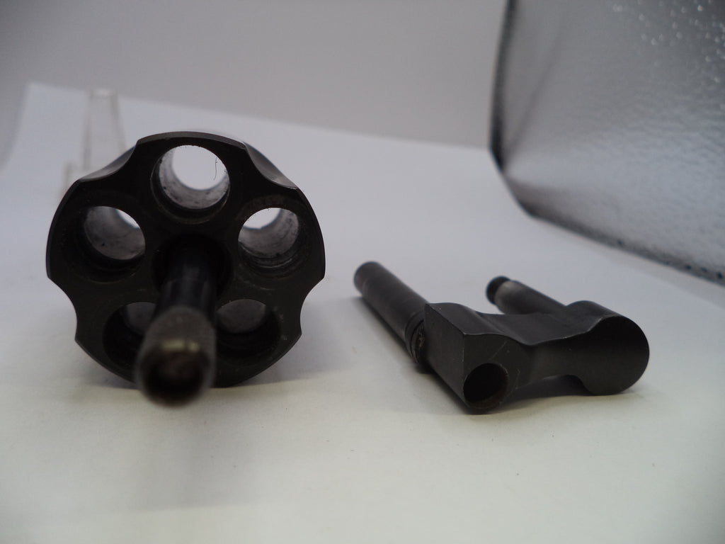 A black metal revolver cylinder and matching barrel assembly photographed on a white surface with a soft gray backdrop.