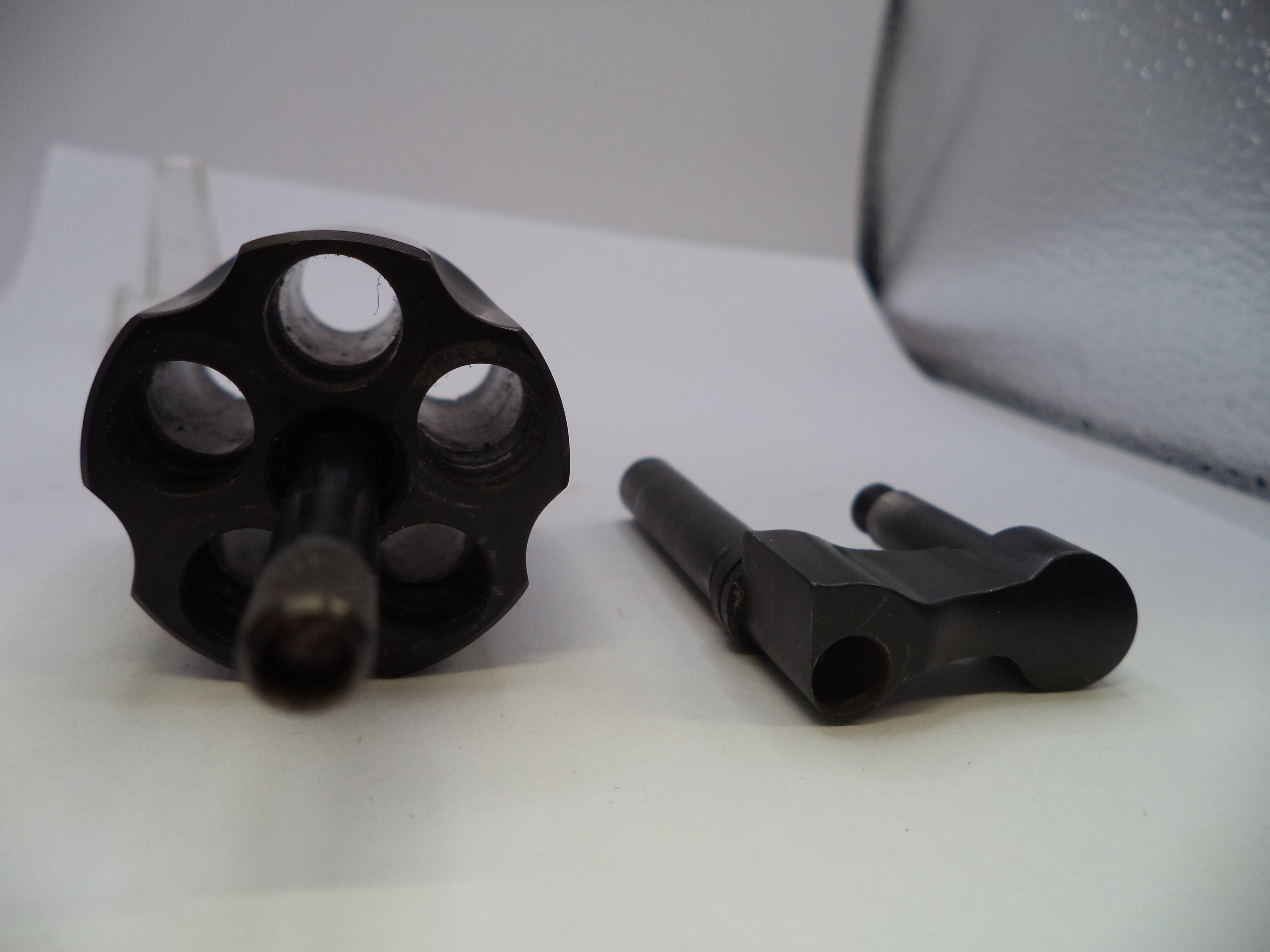 A black metal revolver cylinder and matching barrel assembly photographed on a white surface with a soft gray backdrop.