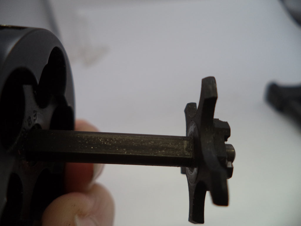 A close-up of a black metal revolver cylinder and barrel shroud held by a hand, showing the exposed barrel pin and pinion gear.