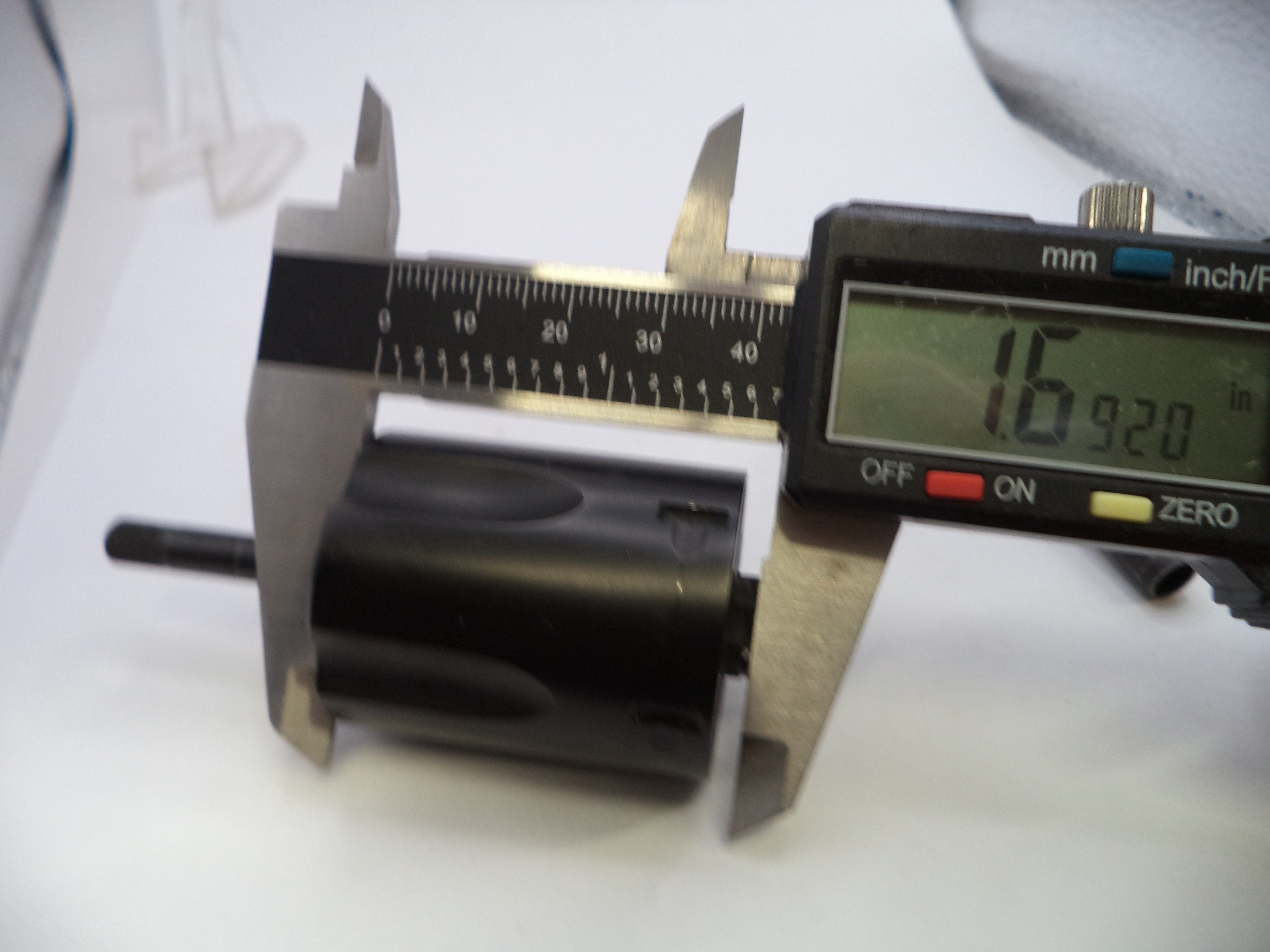 A close-up of a black cylindrical product being measured with a digital caliper, showing a digital readout of 16.920 mm (6.
