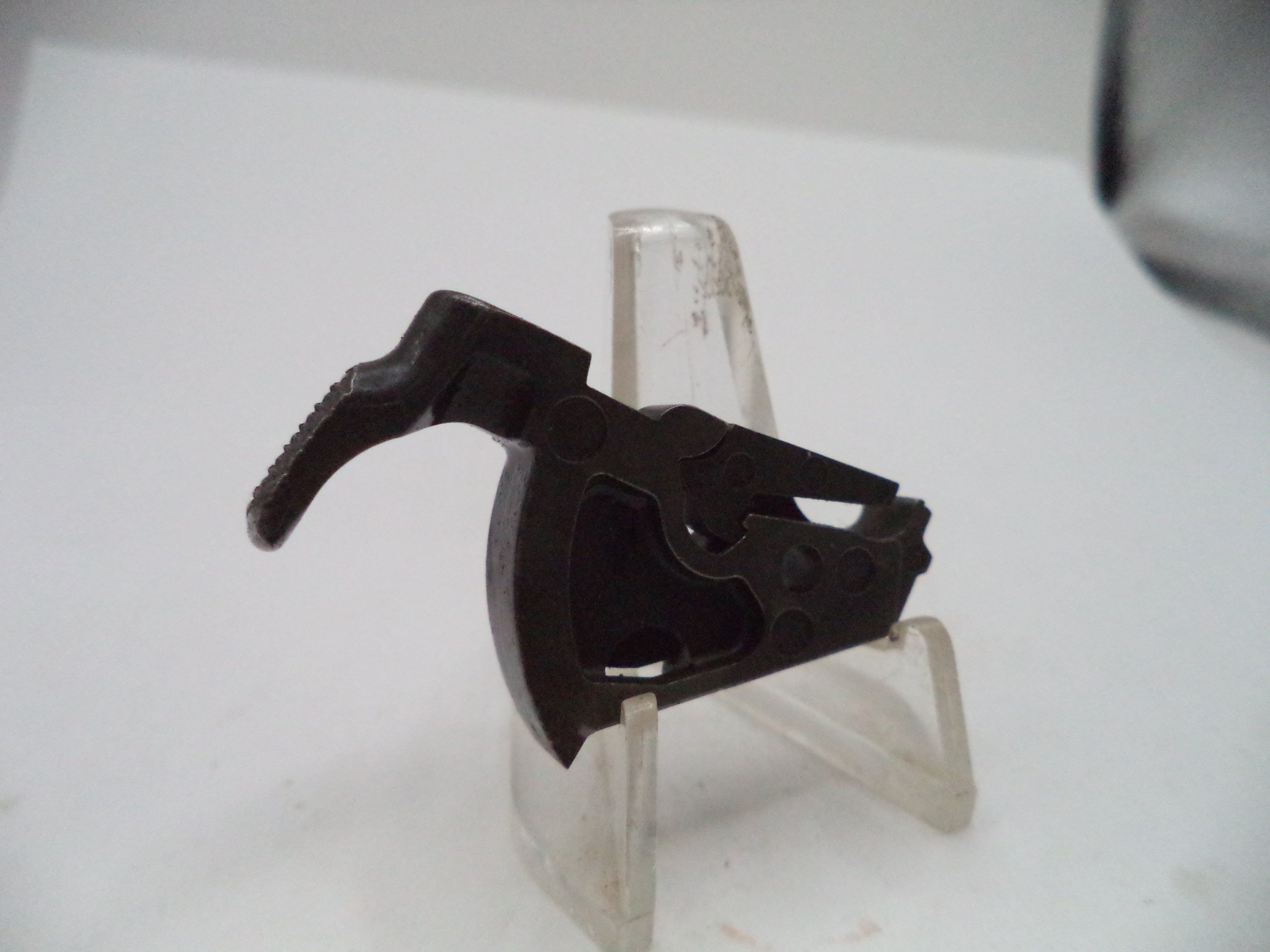 A black plastic trigger assembly for a firearm, displayed on a clear plastic stand against a white background.