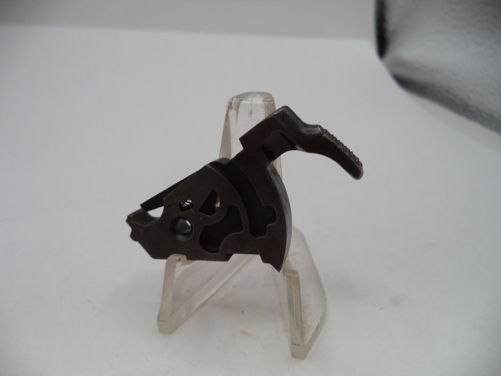 A dark metal firearm trigger assembly with a textured black handle, displayed on a clear plastic stand against a white background.