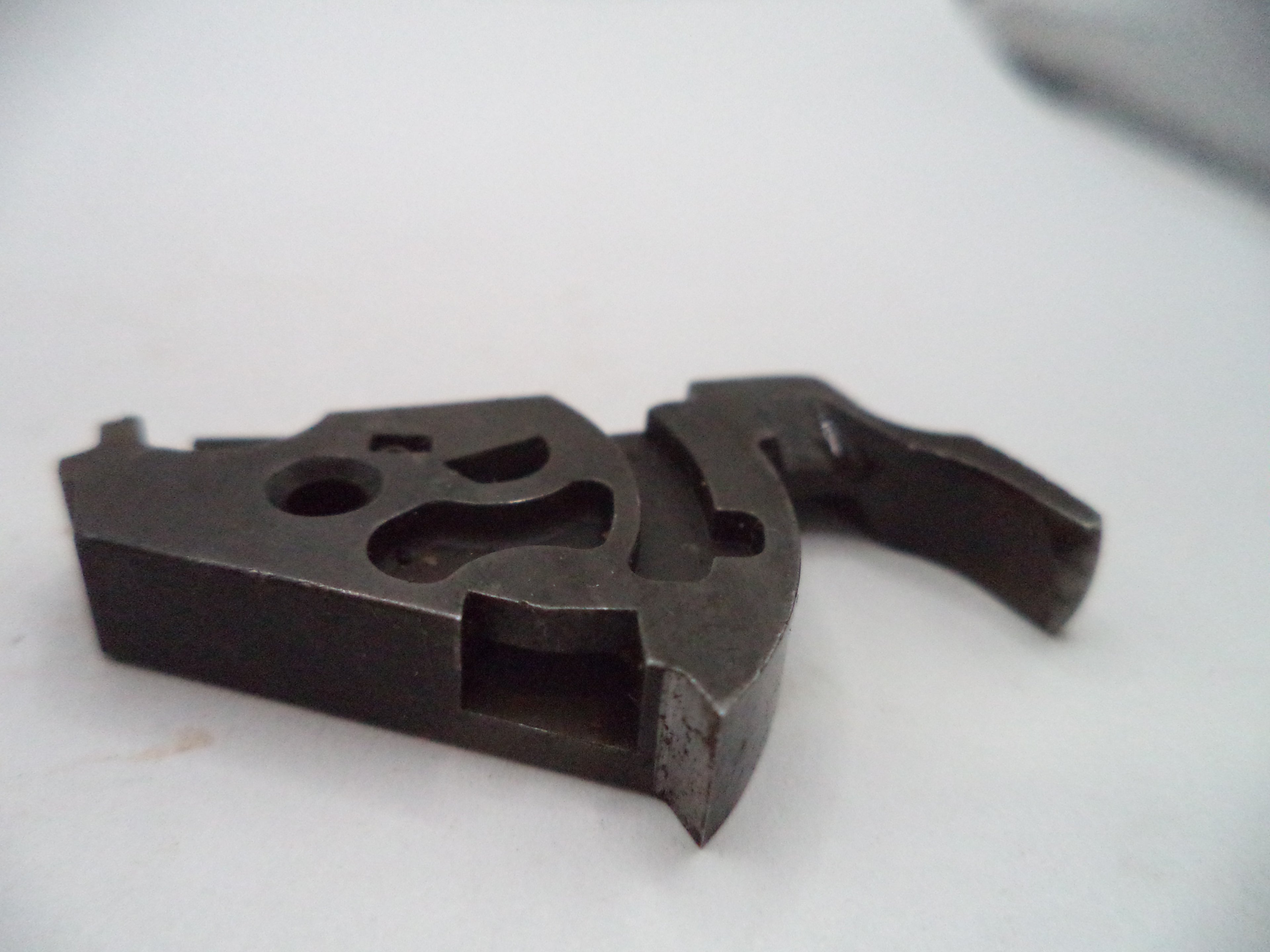A dark metallic gun trigger assembly component, likely a receiver or trigger plate, photographed on a plain white surface.