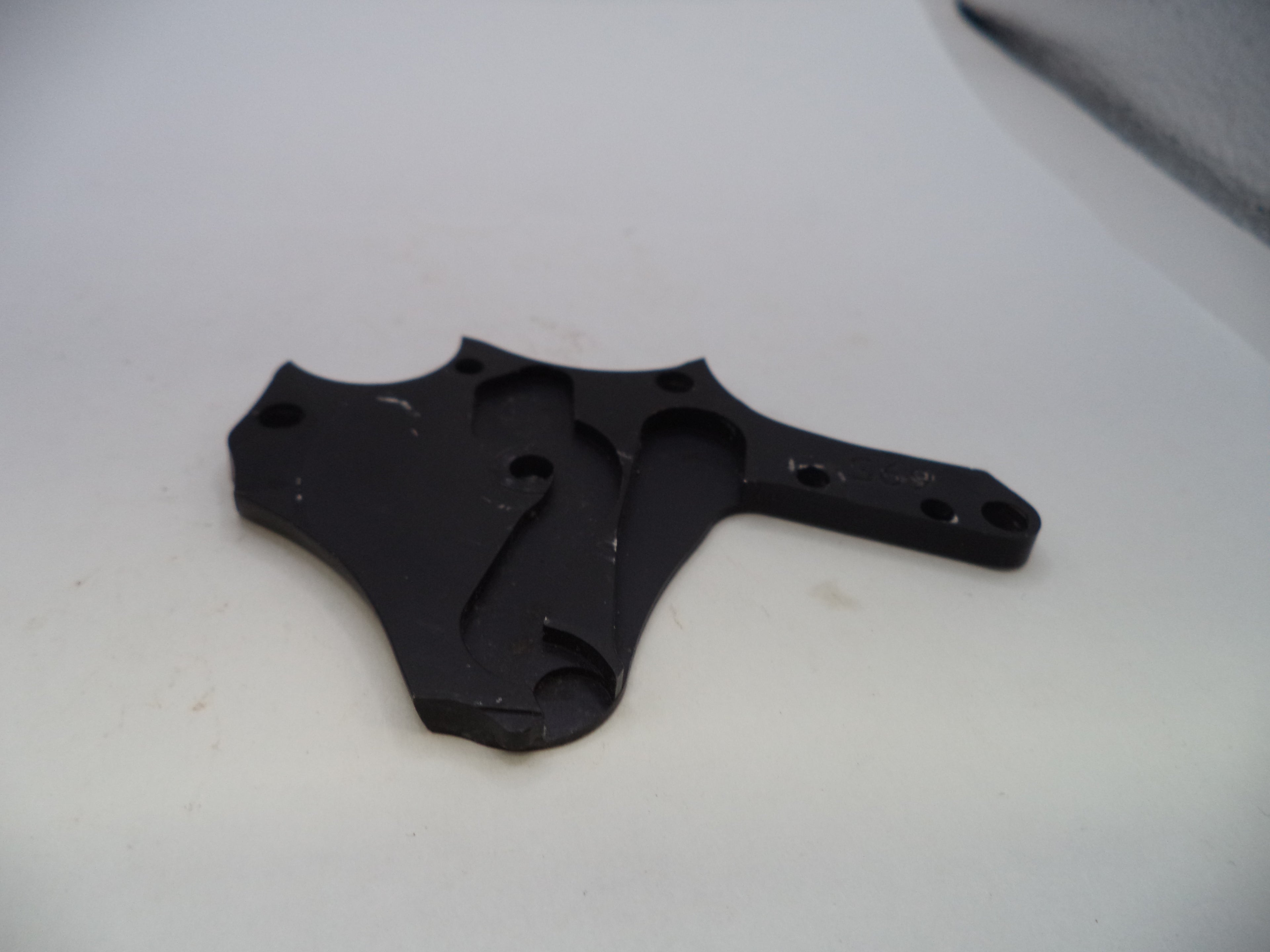 A small black plastic or metal mounting bracket with pre-drilled holes, photographed on a plain off-white surface.