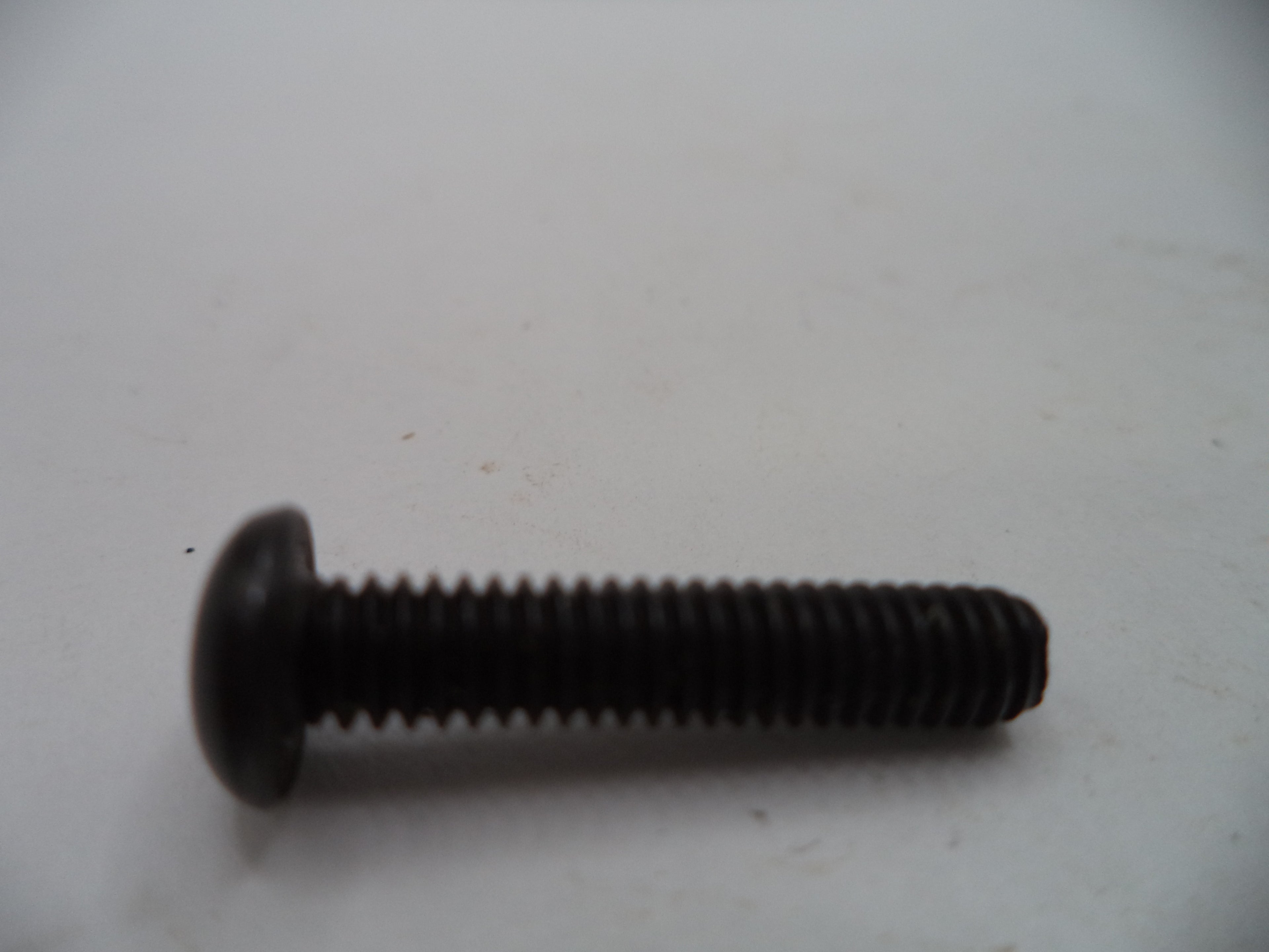 A single black metal flathead screw with a threaded shank, photographed on a plain off-white surface.
