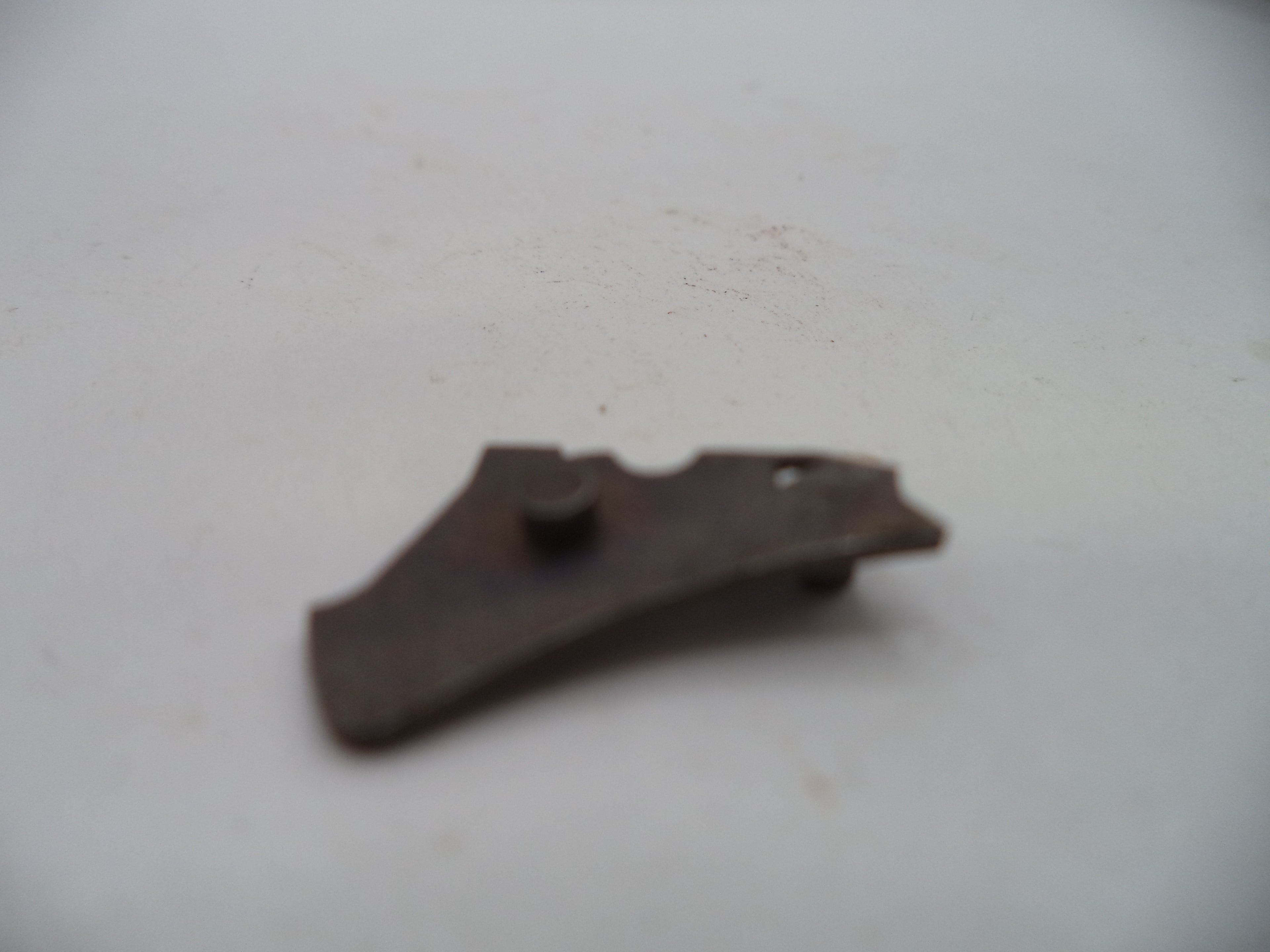 A small, dark brown metal accessory with a textured surface and a central screw, photographed on a plain off-white background.