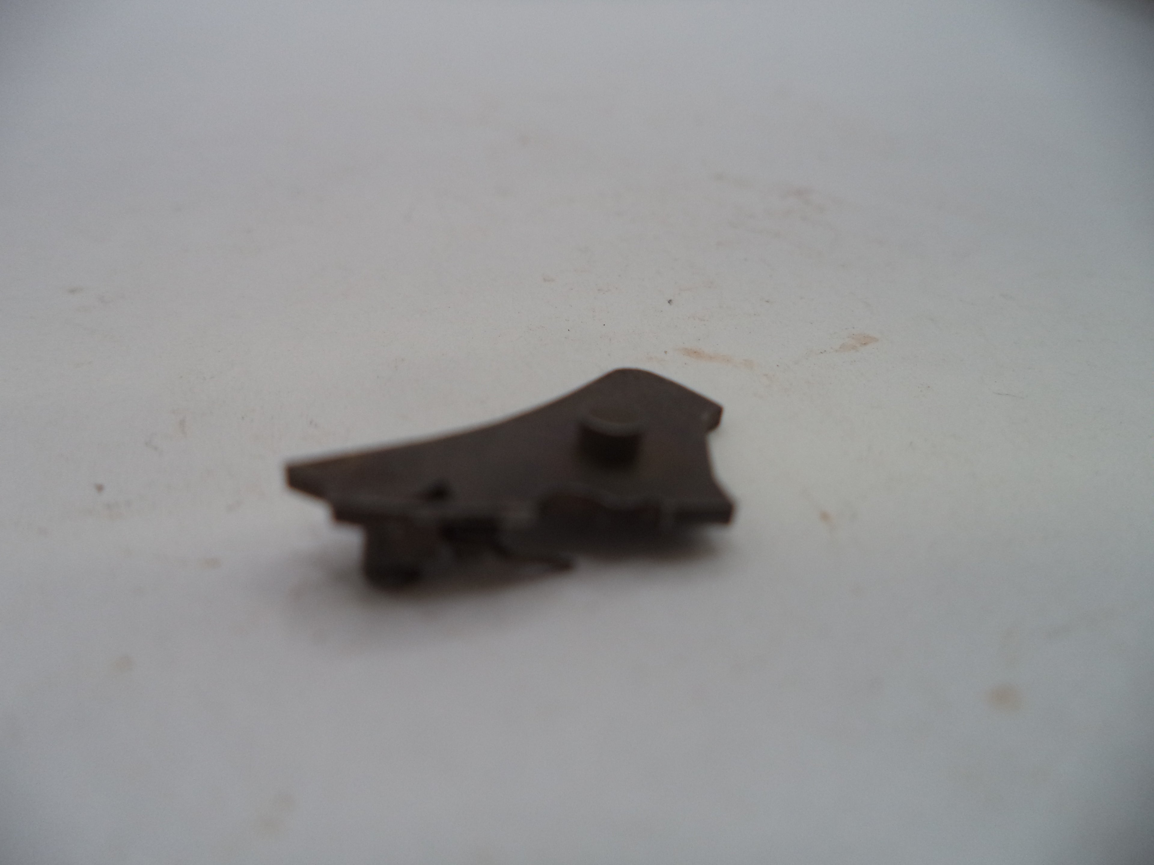 A small dark brown metal hardware component, possibly a latch or bracket, resting on a plain off-white surface.