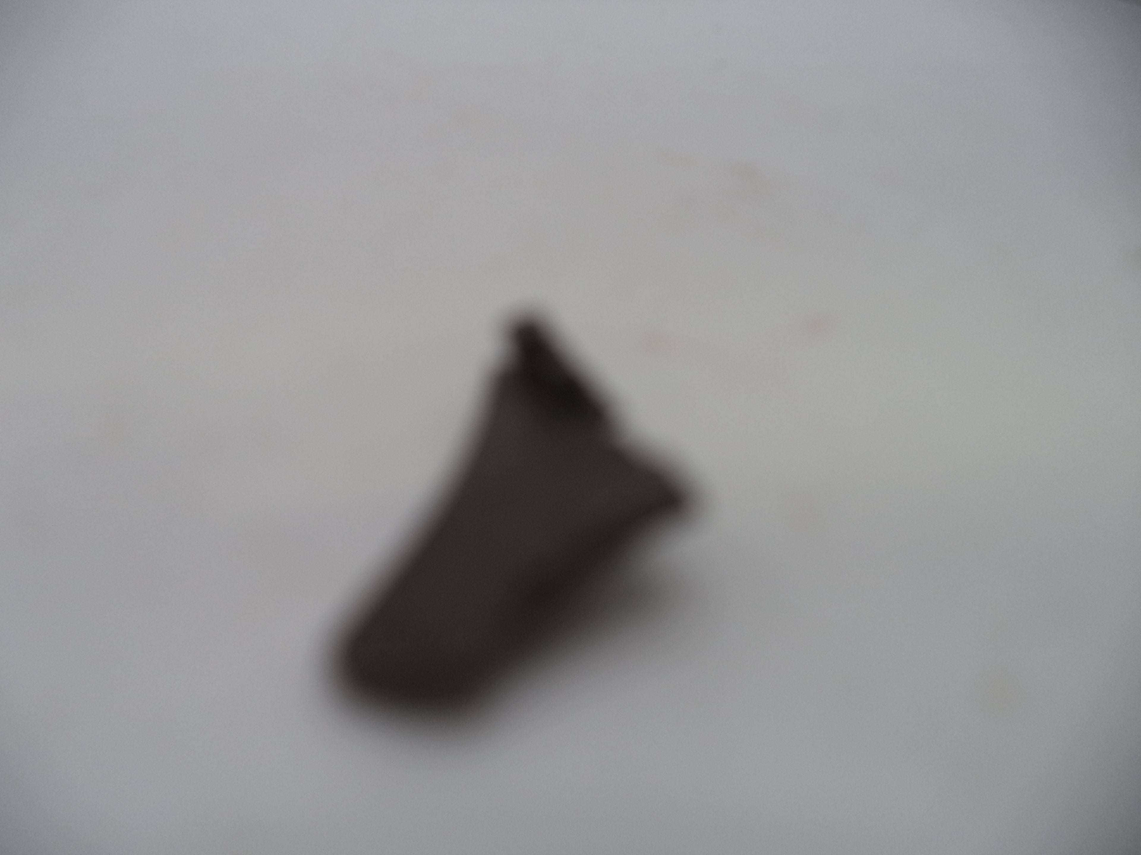 A small, dark brown leather or faux-leather accessory, possibly a strap or clip, shown on a plain off-white background. The image is heavily out of focus, making the details and exact product type highly ambiguous.