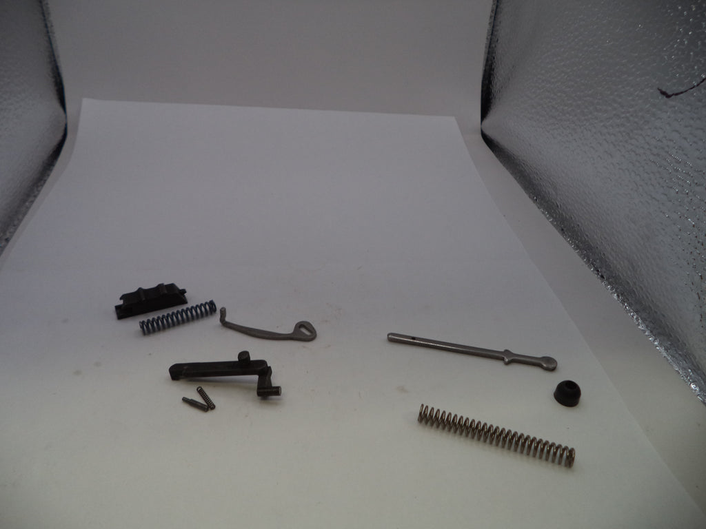 A set of small metal and black mechanical parts, including springs, screws, and small hardware pieces, arranged on a white sheet of paper against a textured lightbox background.