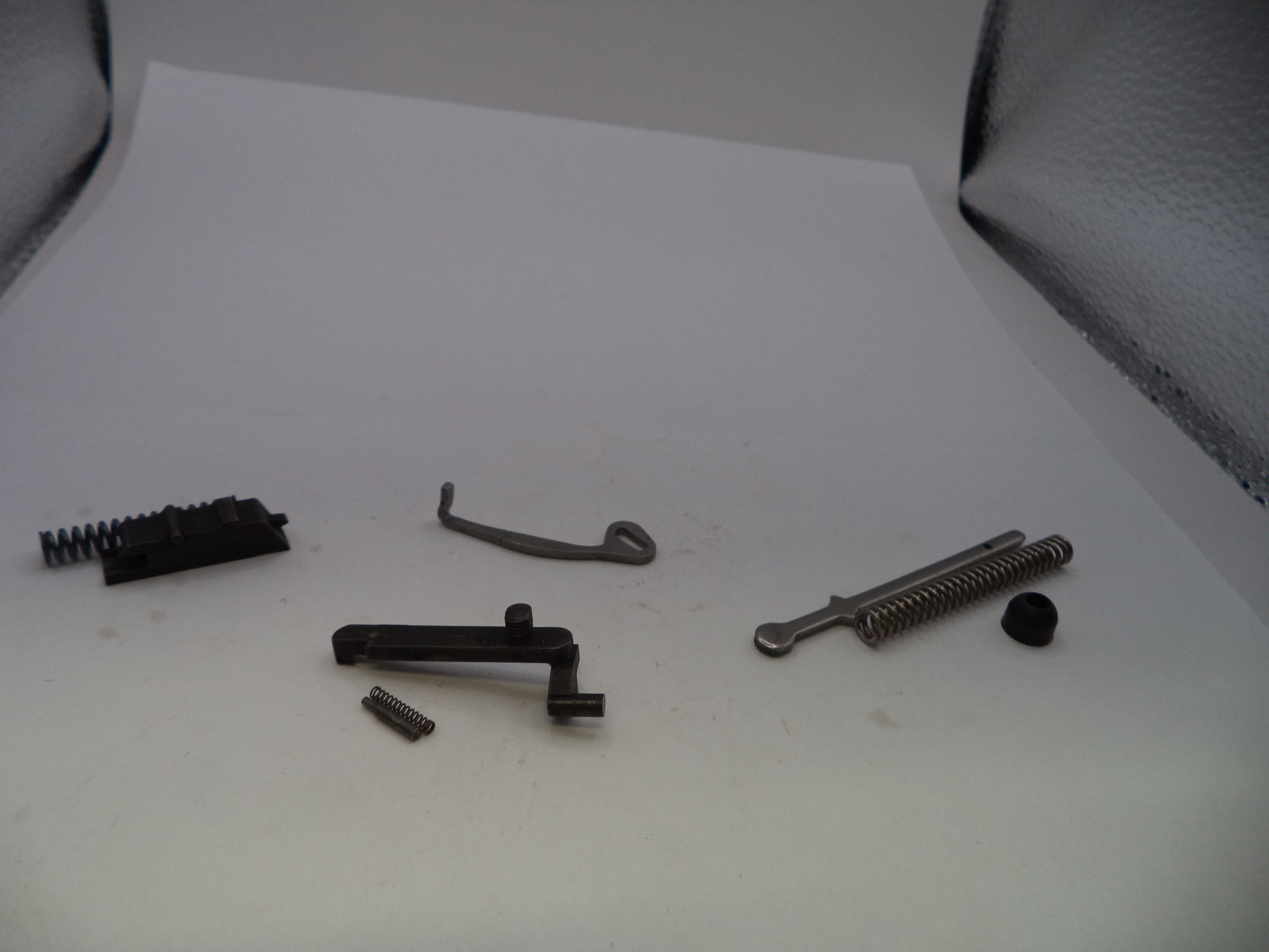 A set of small metal and black mechanical parts, including springs, a lever, and screws, arranged on a white surface.